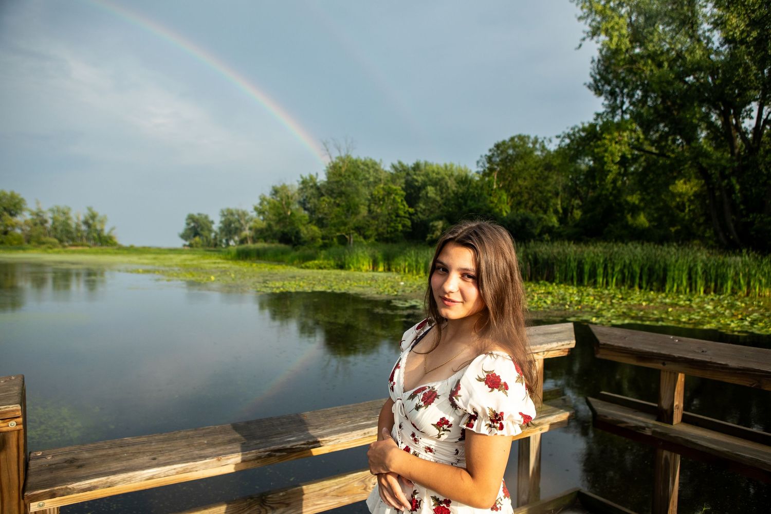 Beautiful rainbow arches over a wooden dock by the water during golden hour.