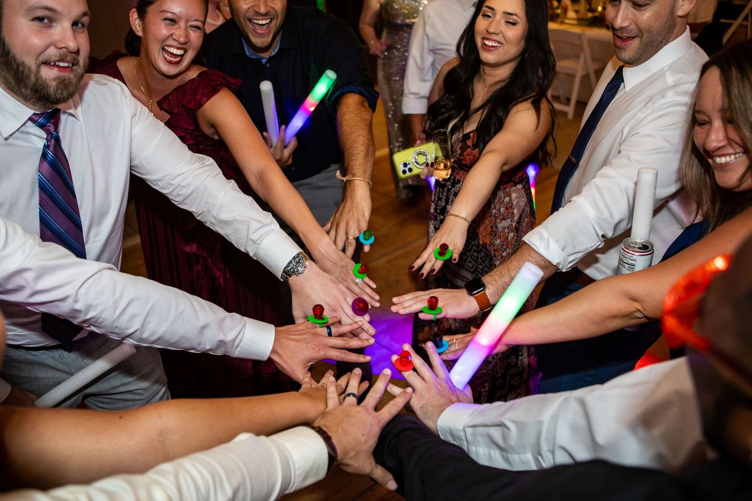 Group of wedding guests holding glowing light sticks together in a circle at a festive reception party.