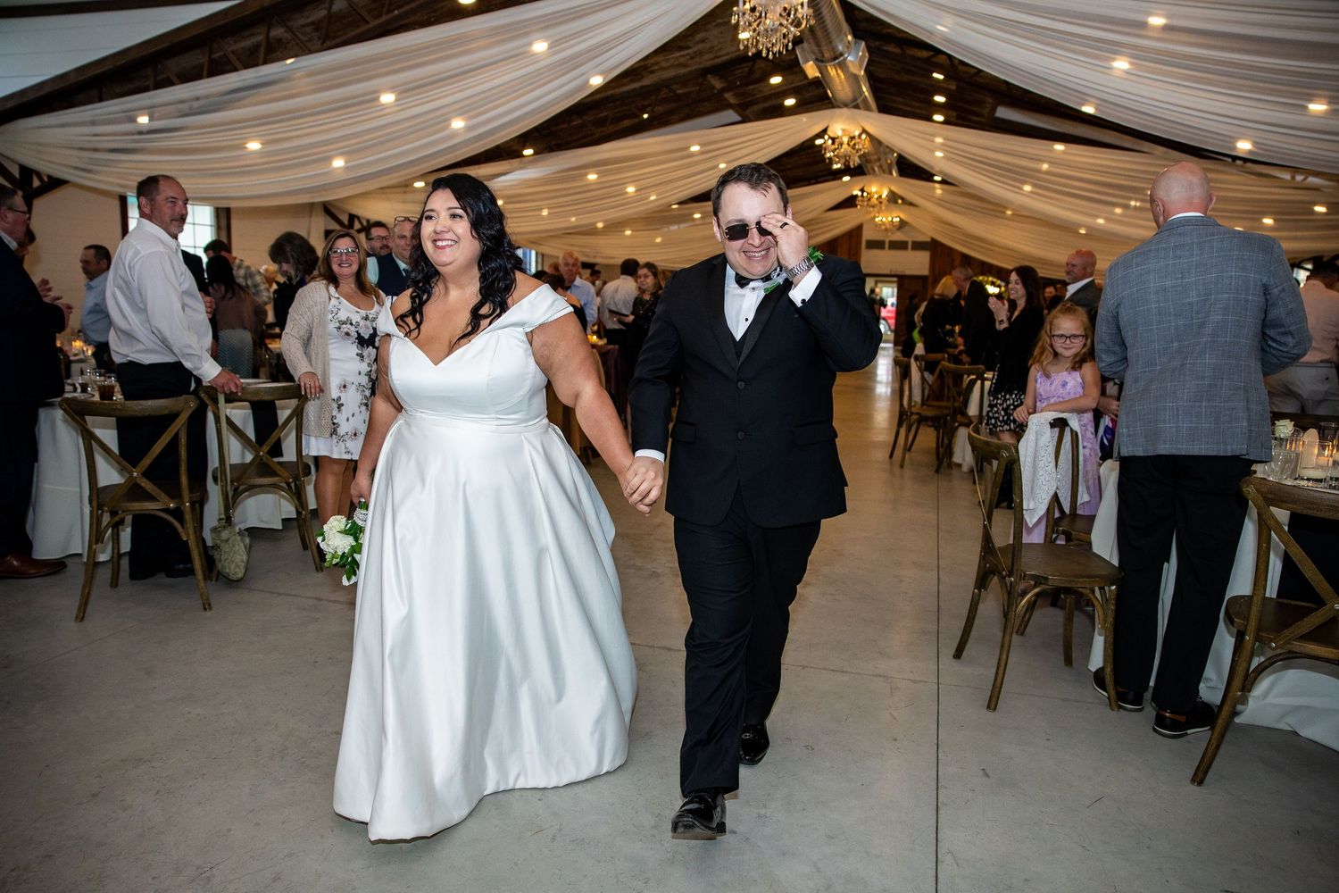 Bride and groom walk hand-in-hand during wedding reception entrance in elegant draped venue.