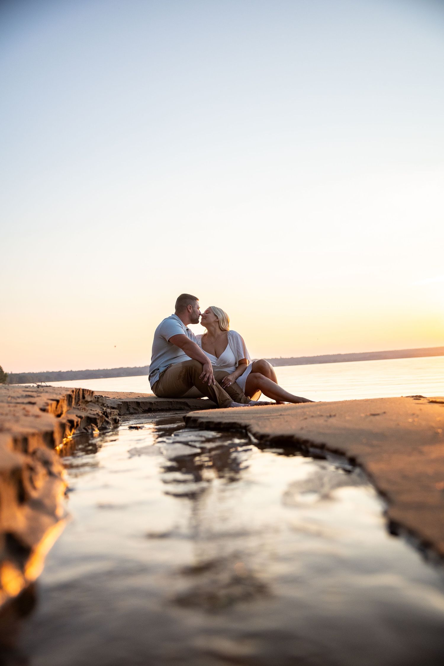 Couple sitting together on a dock at sunset, sharing a romantic moment by the water with golden hour light.