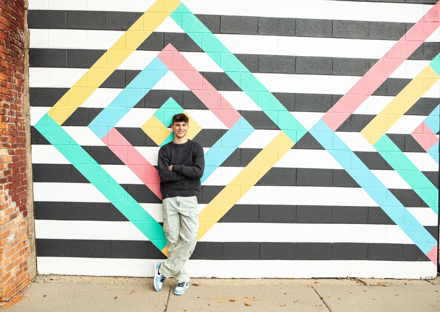 A colorful geometric mural with black and white stripes features intersecting turquoise, yellow and pink diagonal lines on a wall.