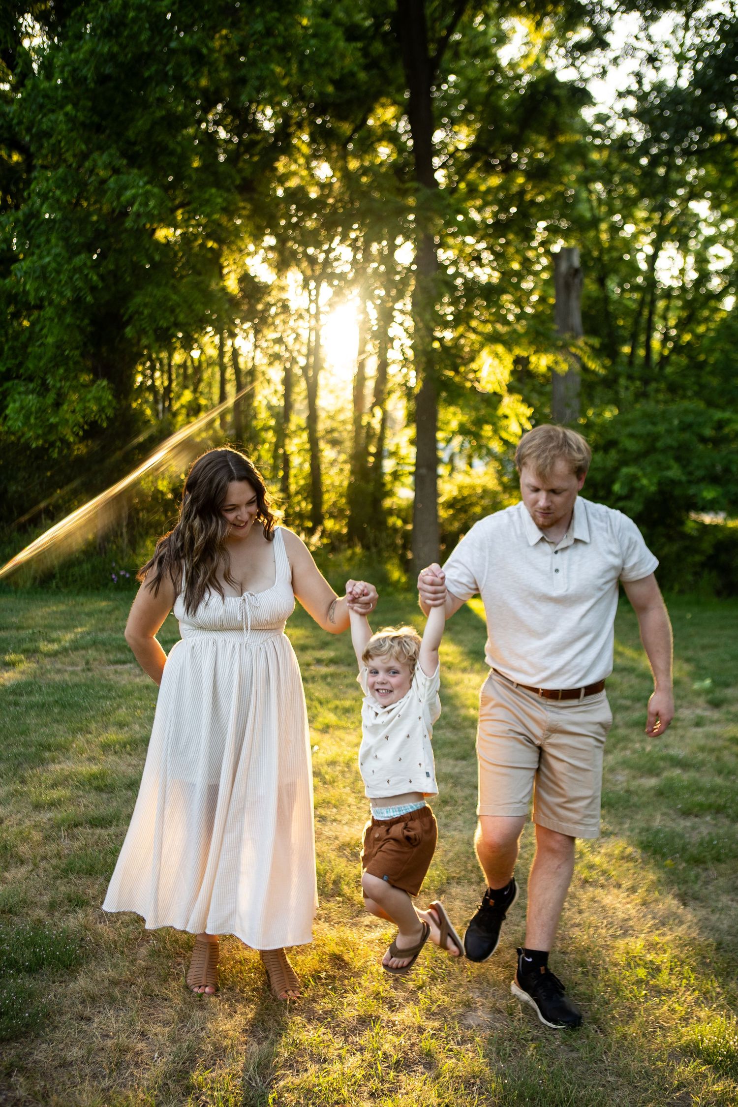Family playing and running together in a sunlit grassy field during golden hour.