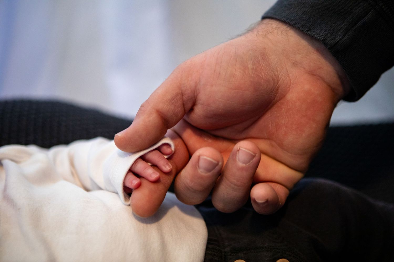 Detail shot of hands gently touching white fabric in dramatic lighting.