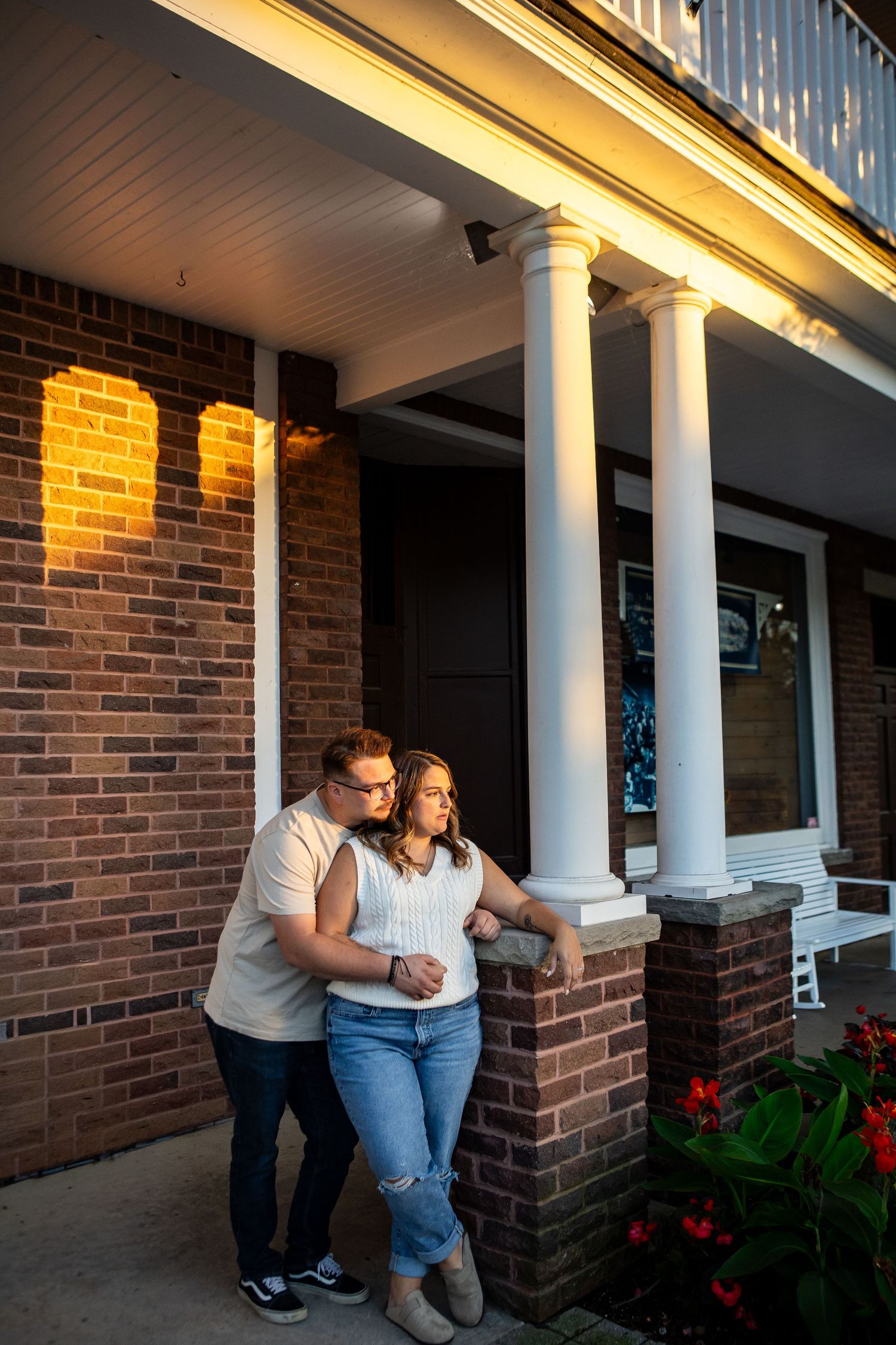 Evening portrait session on a brick porch with white columns and red flowers.