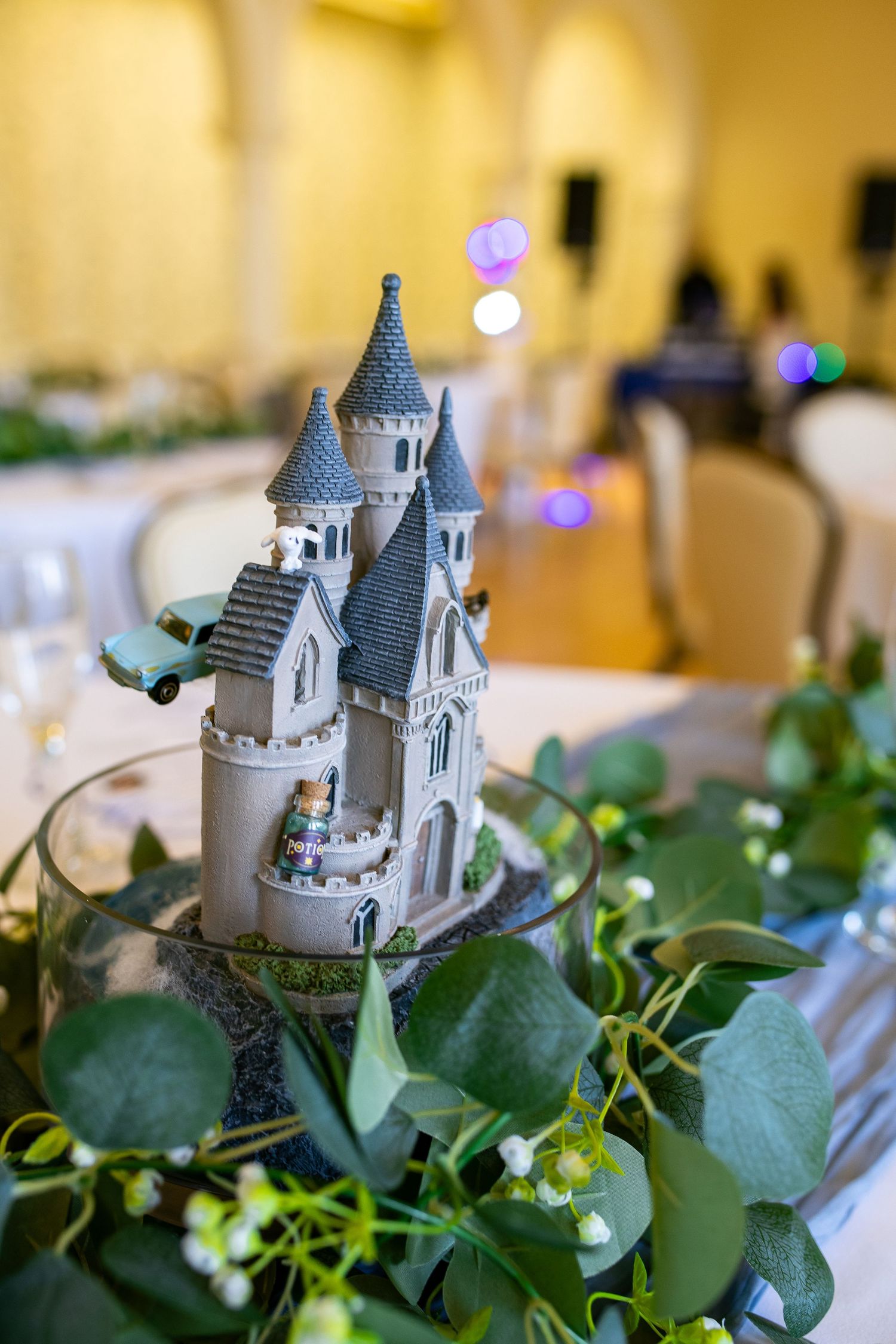 Fairy tale castle centerpiece with greenery on wedding reception table.