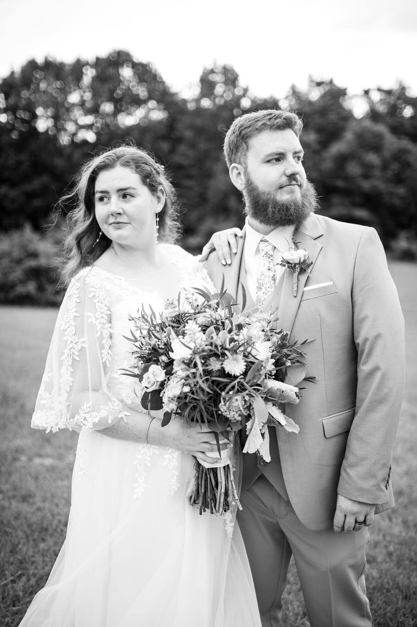 Black and white wedding portrait showing couple embracing outdoors with elegant floral bouquet.