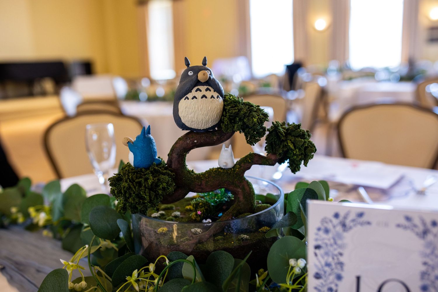 Totoro figurine centerpiece on a moss-covered bonsai tree at a Studio Ghibli themed wedding reception.