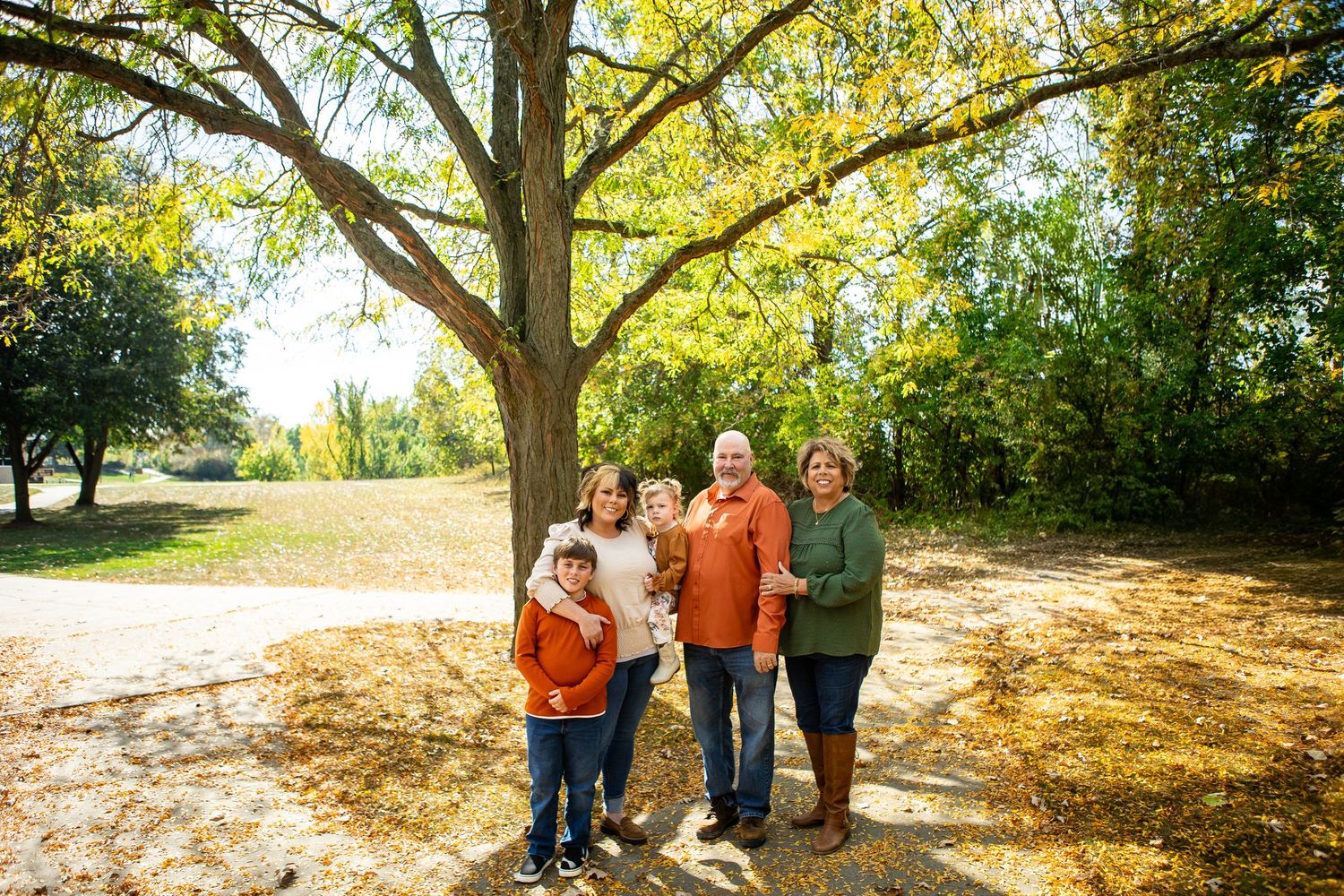 Extended family gathering under large trees for outdoor group photos in golden sunlight.