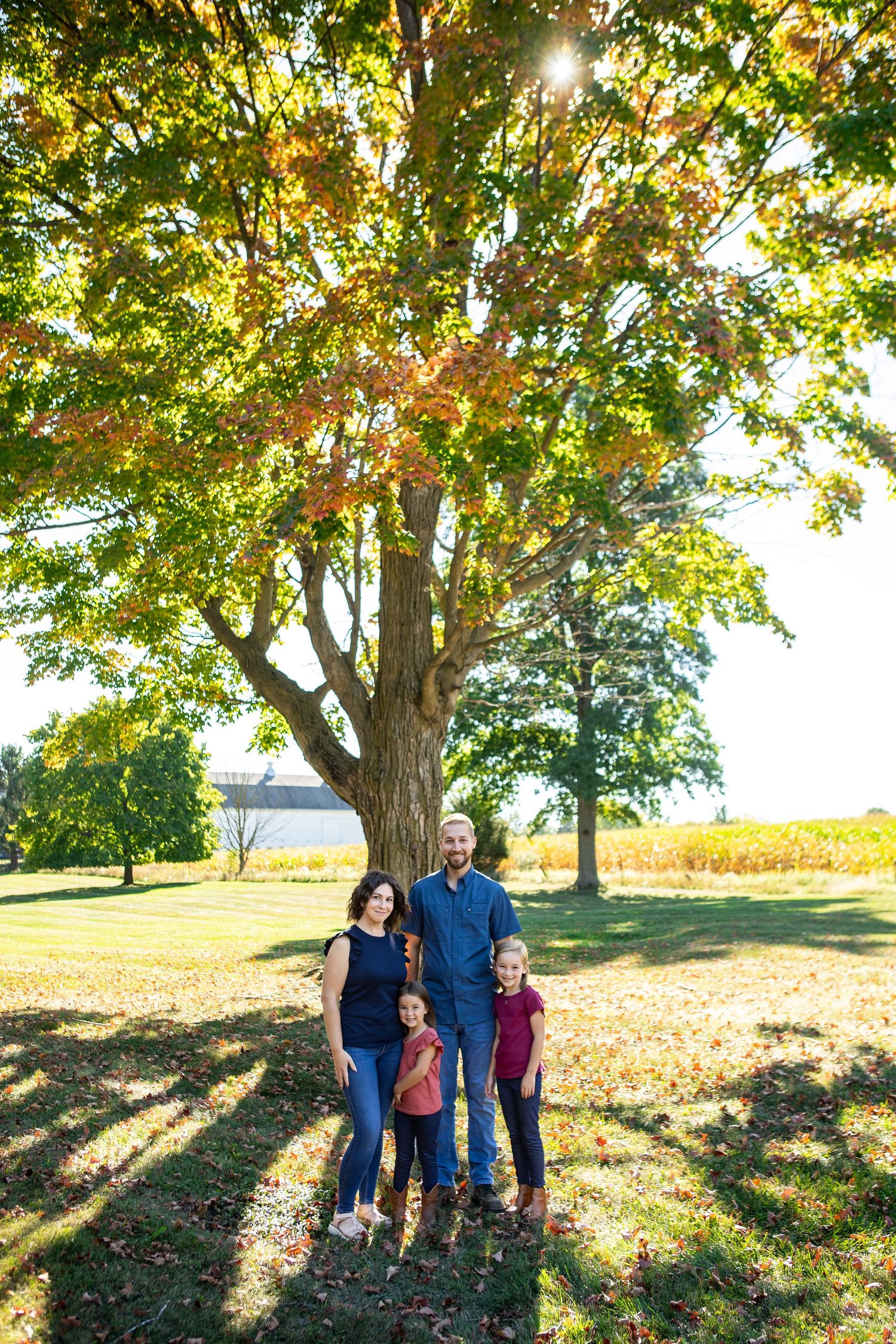 A family poses beneath a large tree with golden sunlight streaming through the branches.