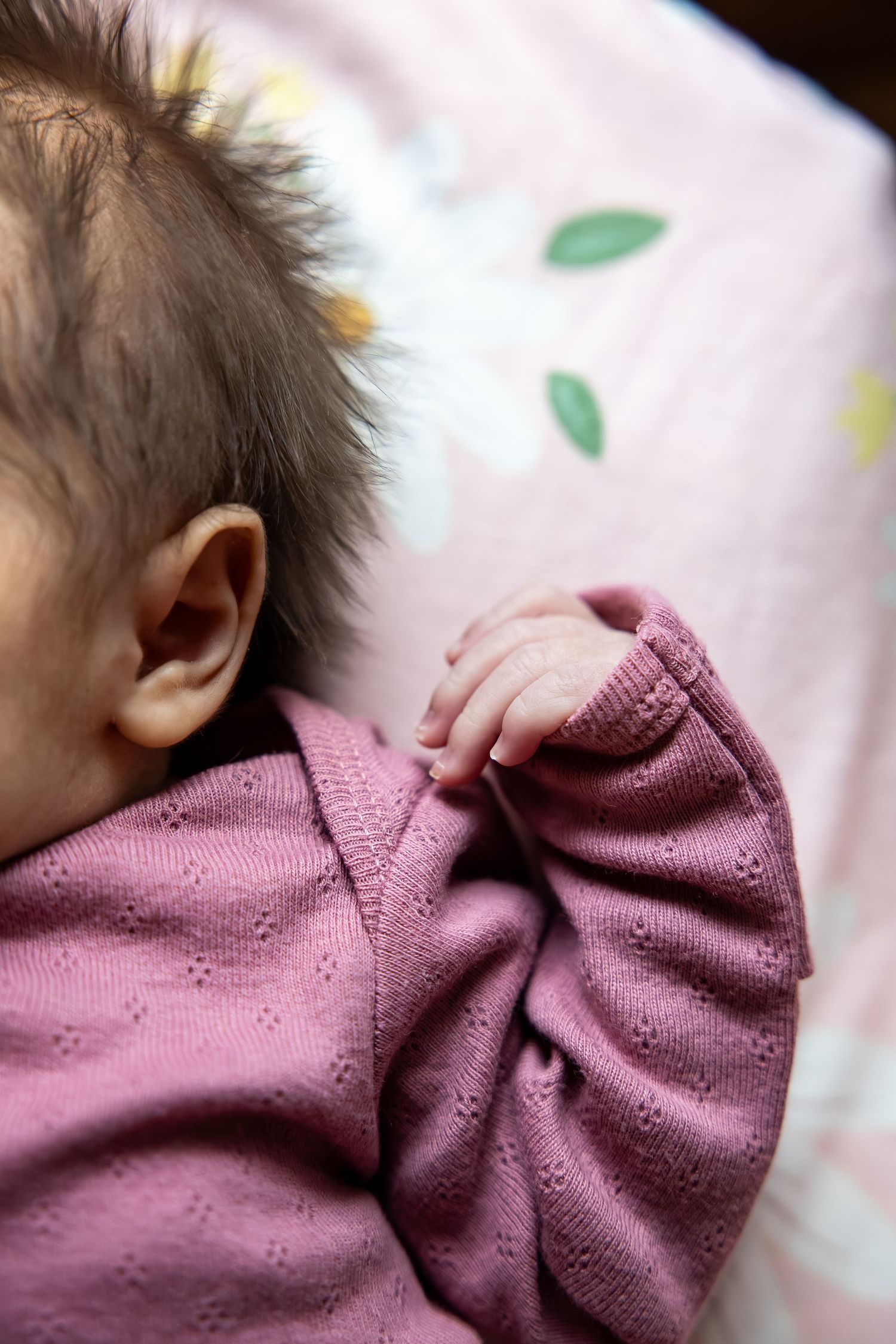 Close-up of a sleeping newborn baby in a pink onesie lying on a floral blanket.