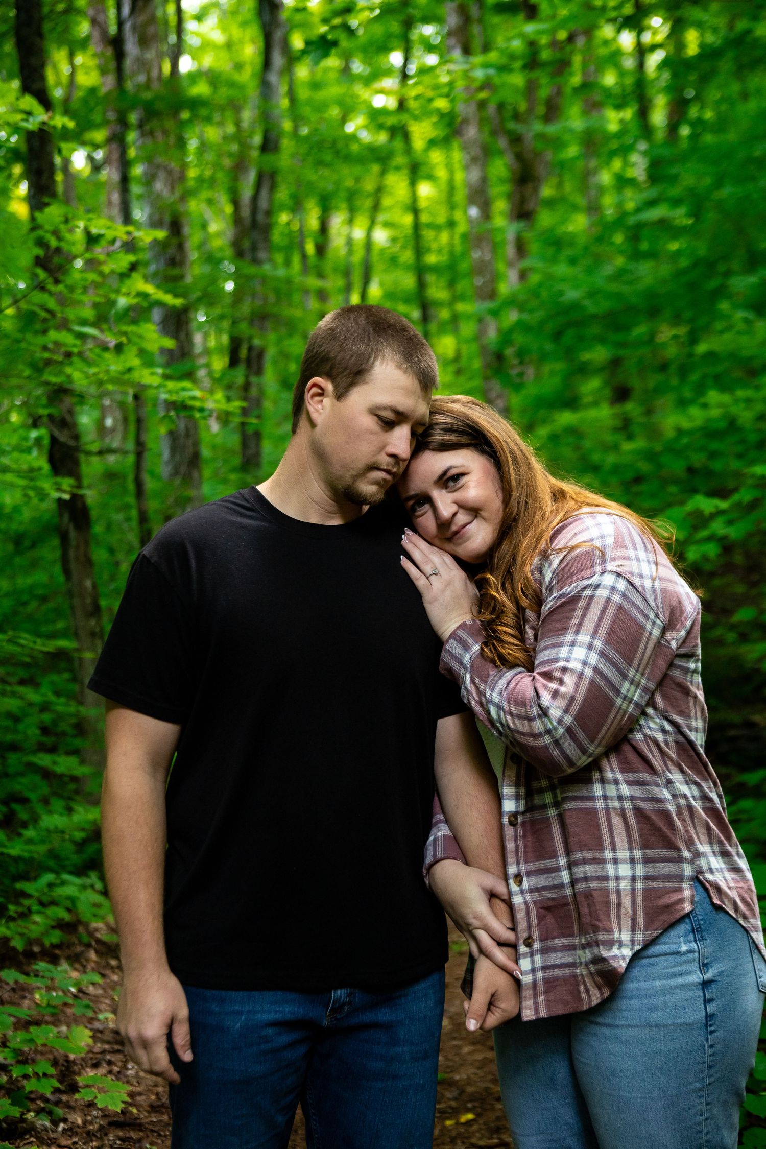 A couple shares an intimate moment on a forest path surrounded by green trees.