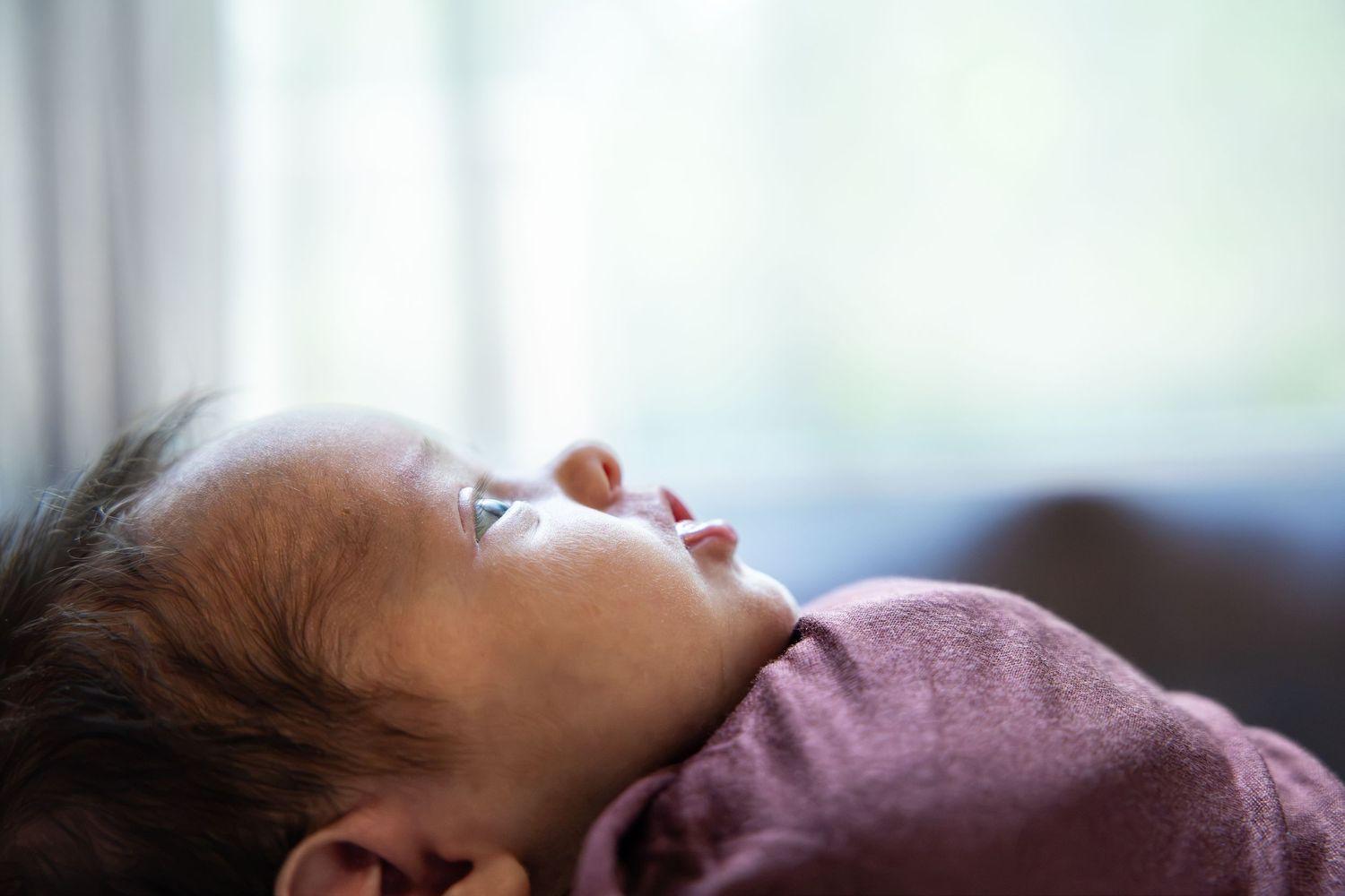 Close-up of a peaceful newborn baby lying down, gazing upward in soft natural light.