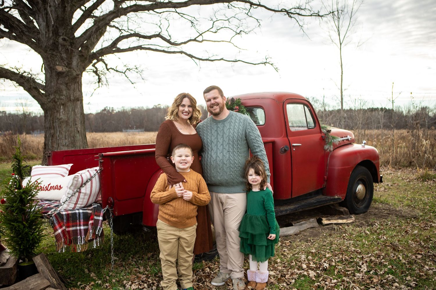 A vintage red pickup truck serves as a rustic backdrop for a casual outdoor photo session in a rural setting.