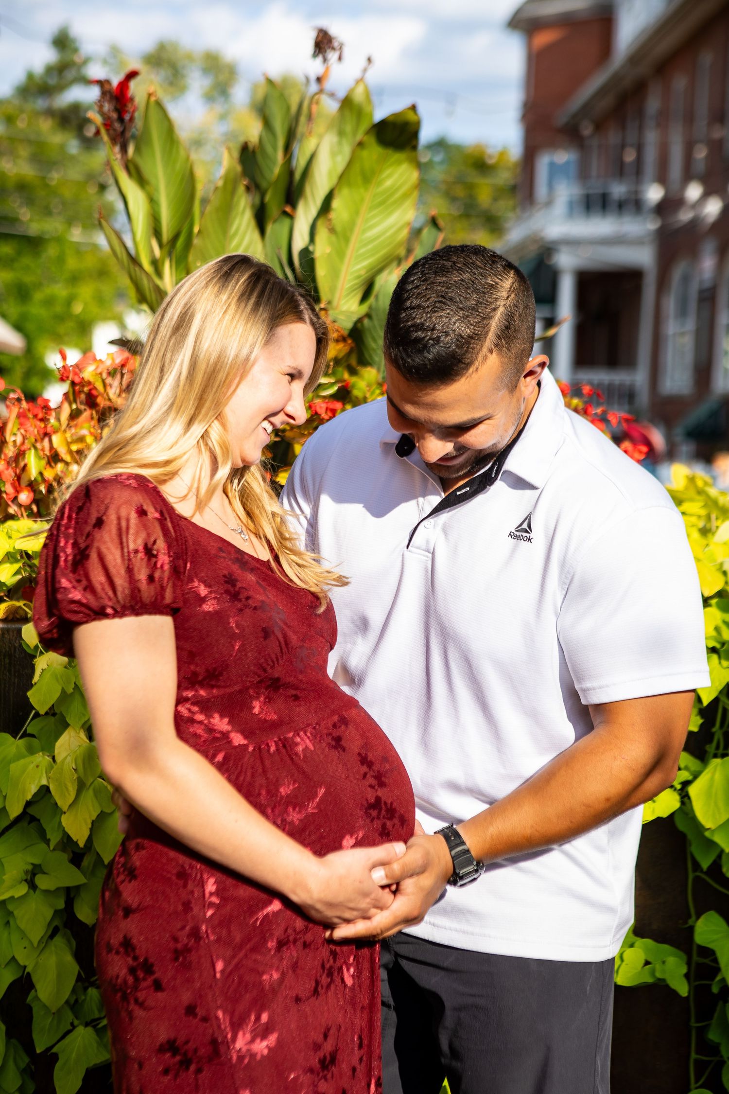Expectant couple in a garden setting with red dress and white polo shirt.