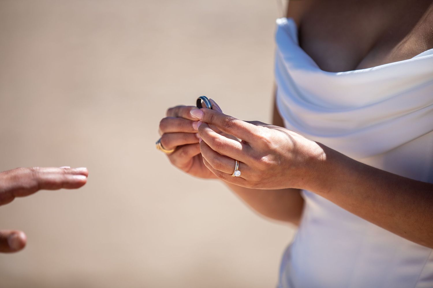 Close-up of a woman in a white dress holding a ring during a beach wedding ceremony.