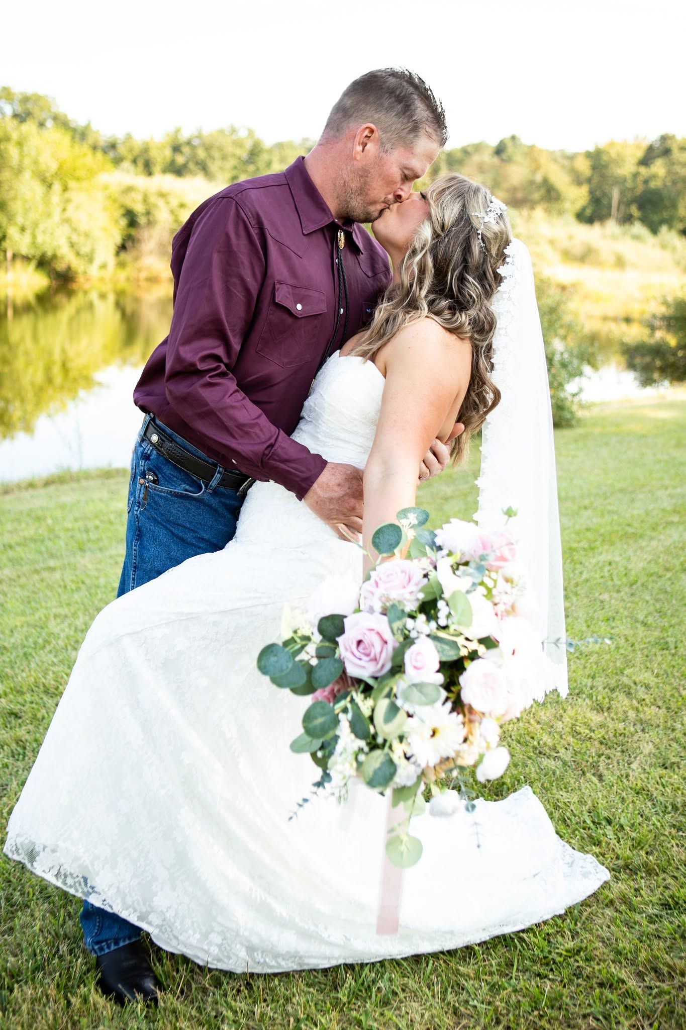 Romantic wedding portrait in sunlit field with white dress and floral bouquet.