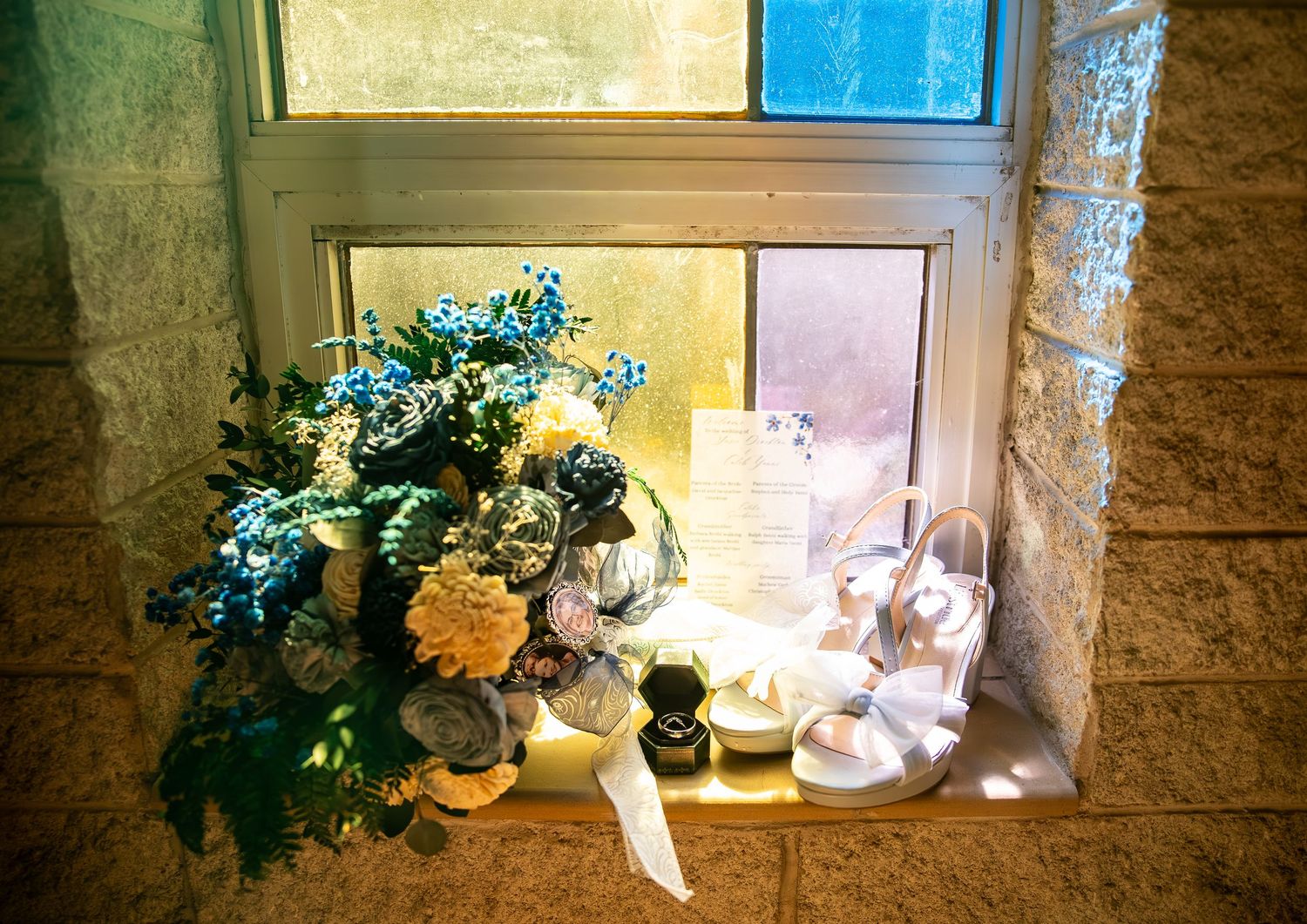 Floral arrangement with blue and white flowers displayed on a sunlit windowsill with candles and decorative items.