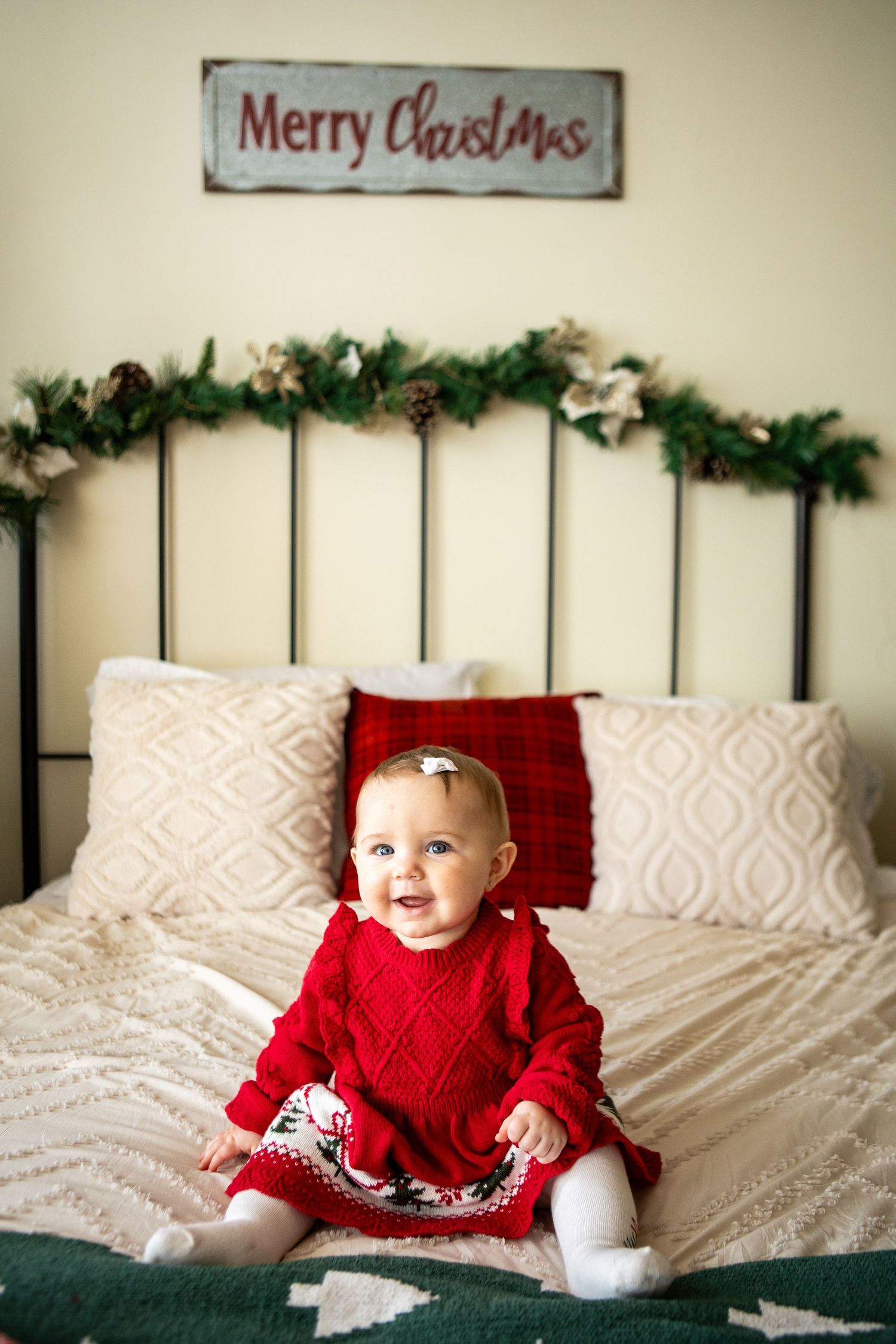 A series of four holiday photos showing a baby in a red sweater on a white bed with Christmas decorations in the background.