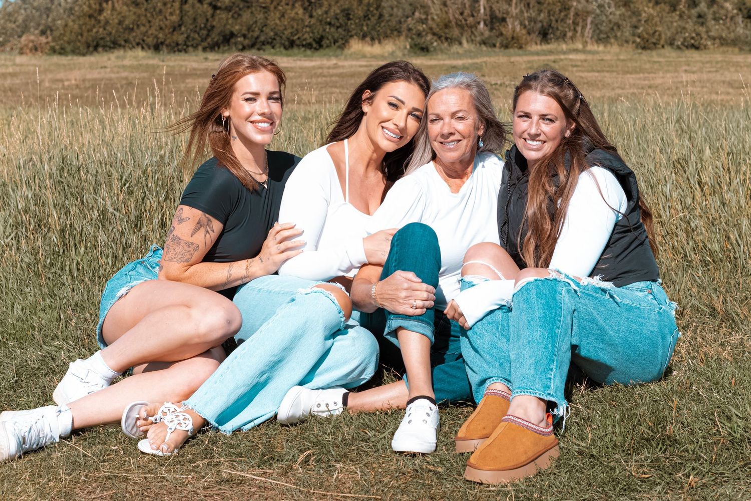 Group portrait of women from different generations sitting together in a grassy field during a family session.