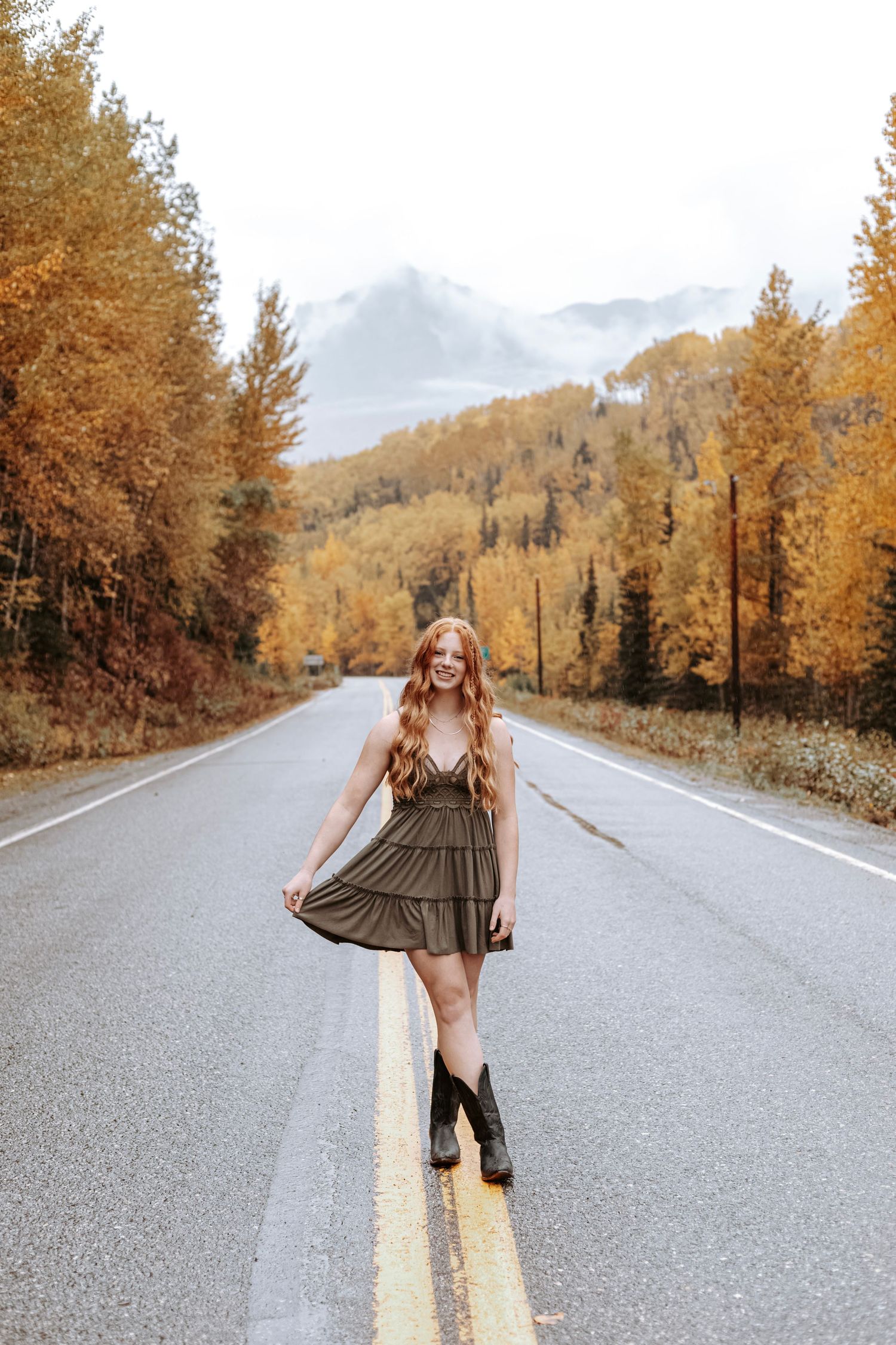 Outdoor senior portrait of a young woman in the middle of a road with trees and mountain backgrounds