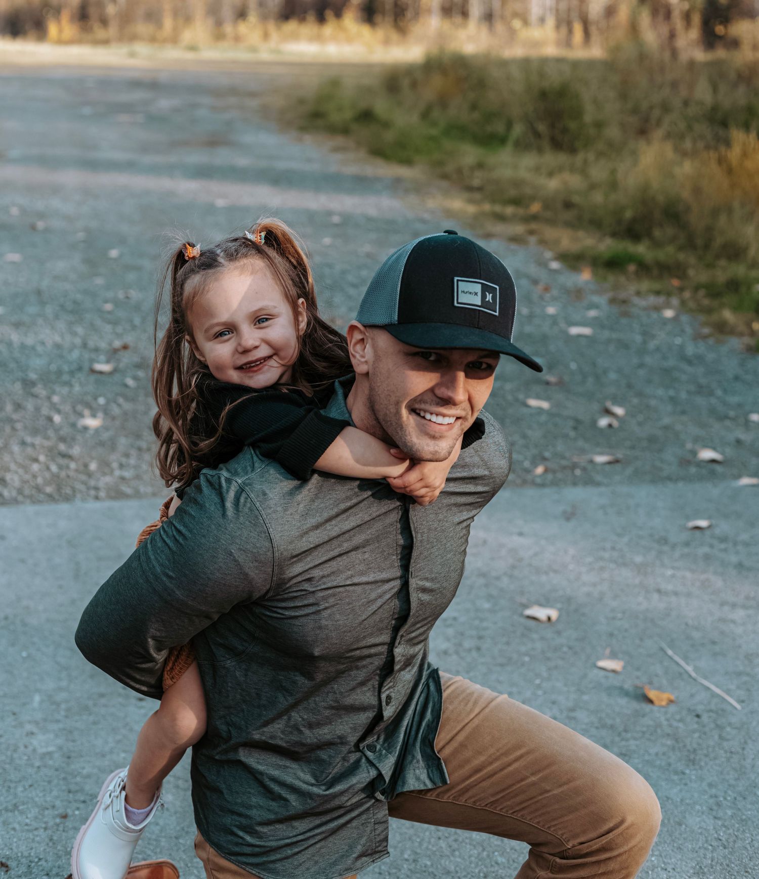 Smiling dad giving his daughter a piggyback ride during a fall family session on a trail in Alaska – candid lifestyle photography
