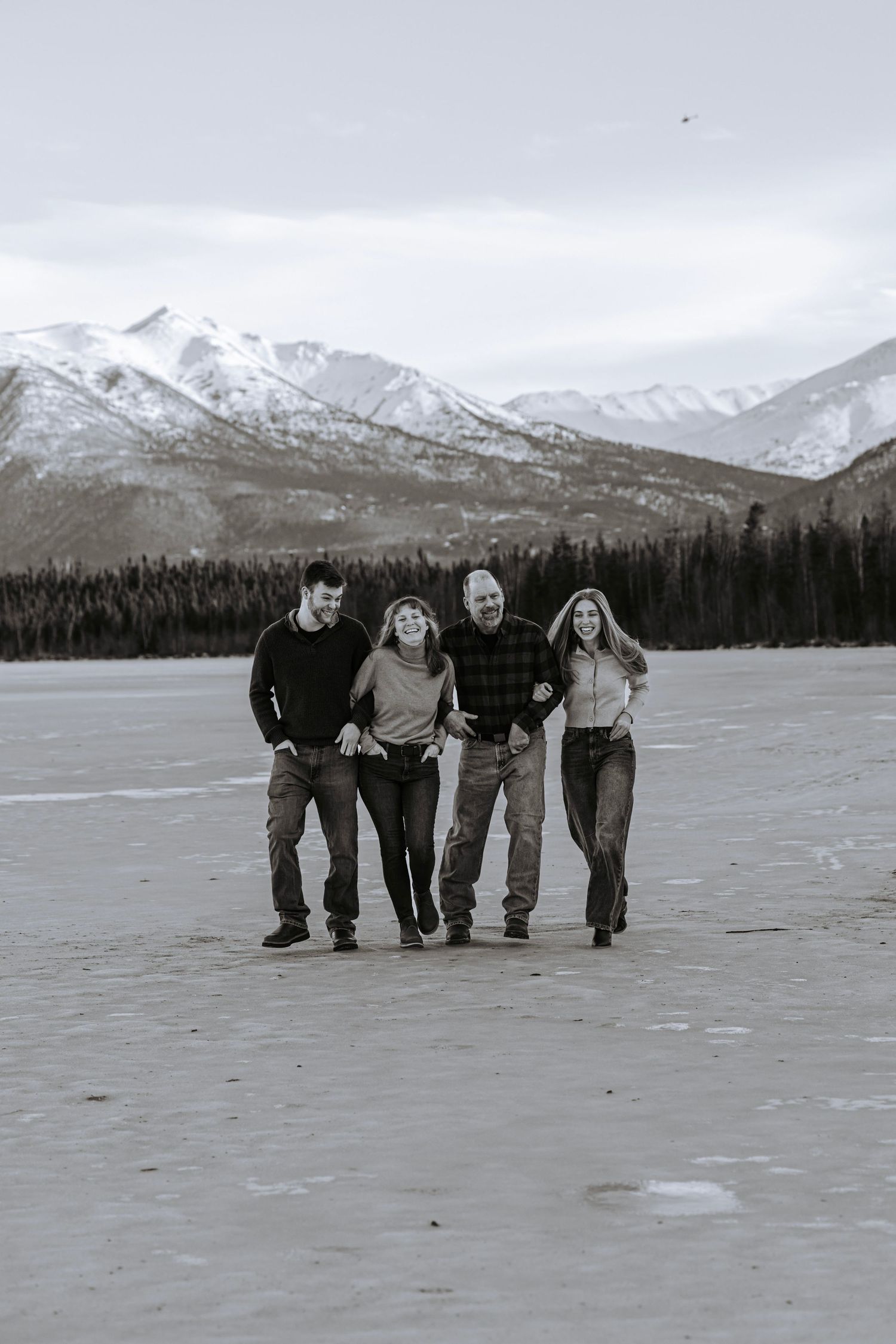 Black and white portrait of a family of four laughing and walking on ice with a mountain background