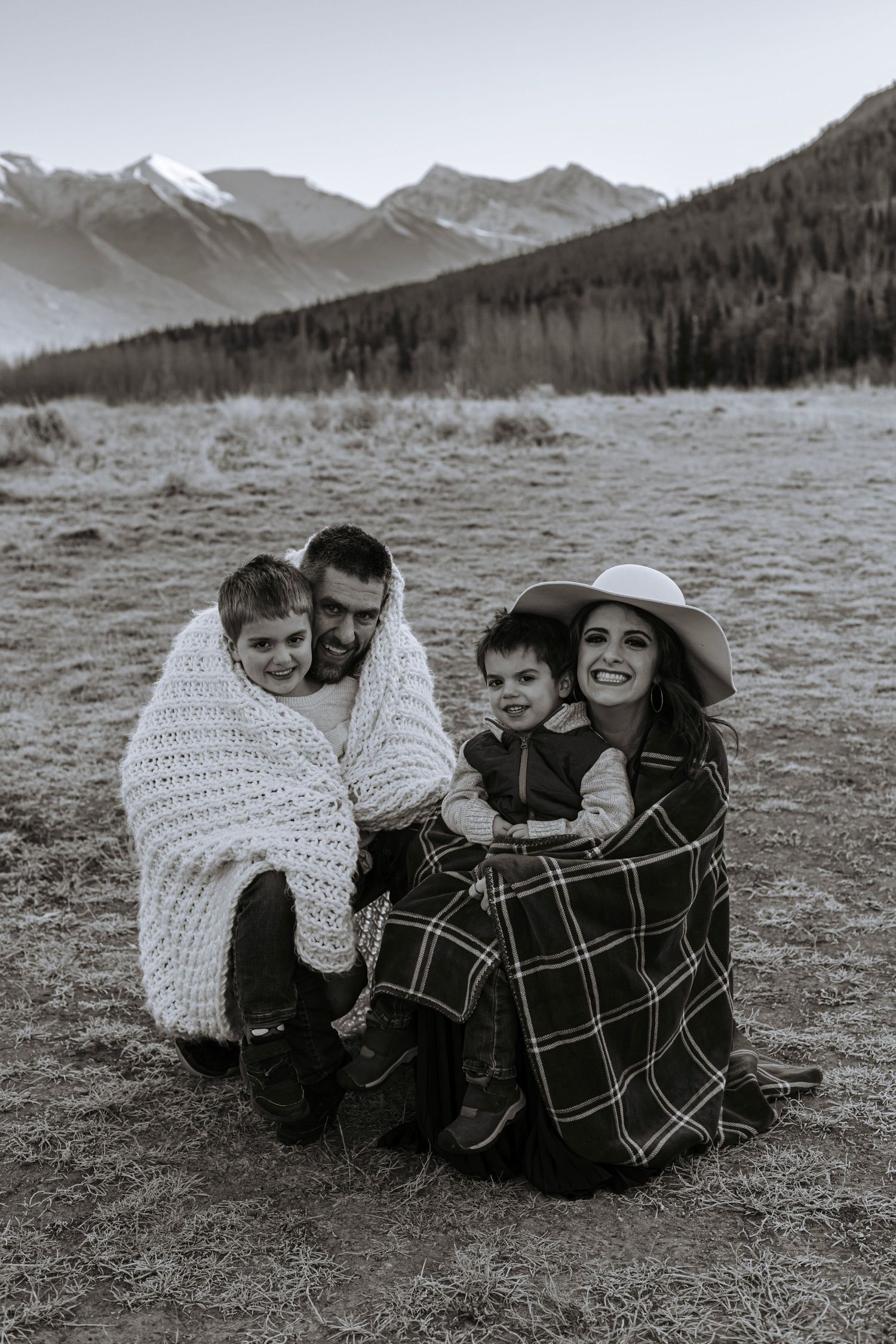 Black and white family portrait of parents and children wrapped in blankets with Alaskan mountain scenery behind them.