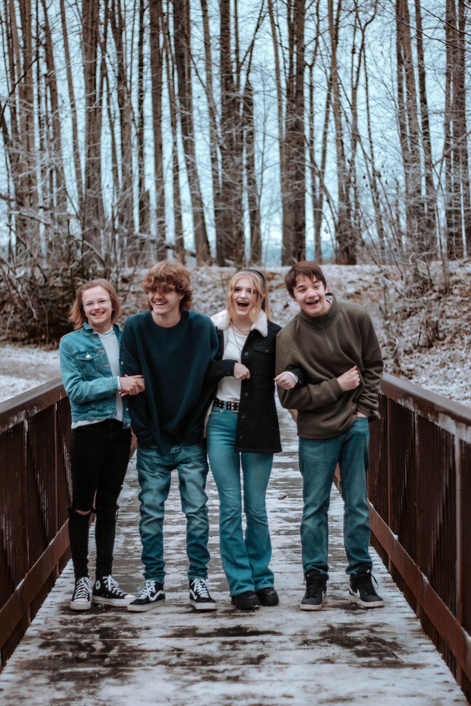 Group of siblings laughing together on an Alaskan wooden bridge during a relaxed outdoor family session.