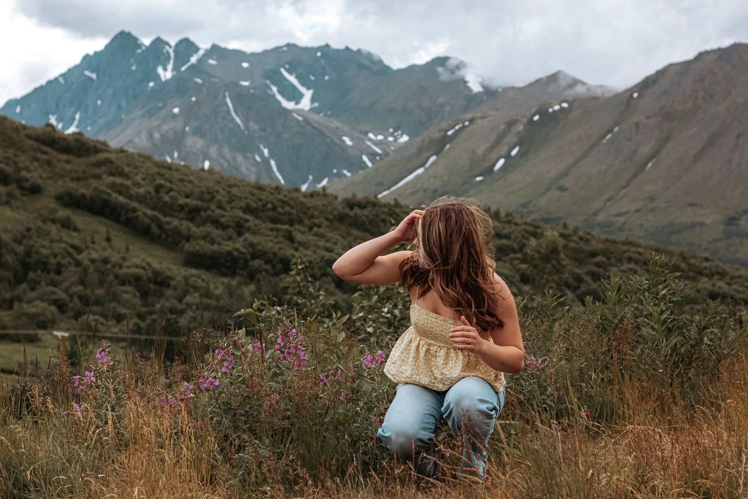 Senior portrait of a young woman kneeling in an Alaskan mountain field during an outdoor senior session.