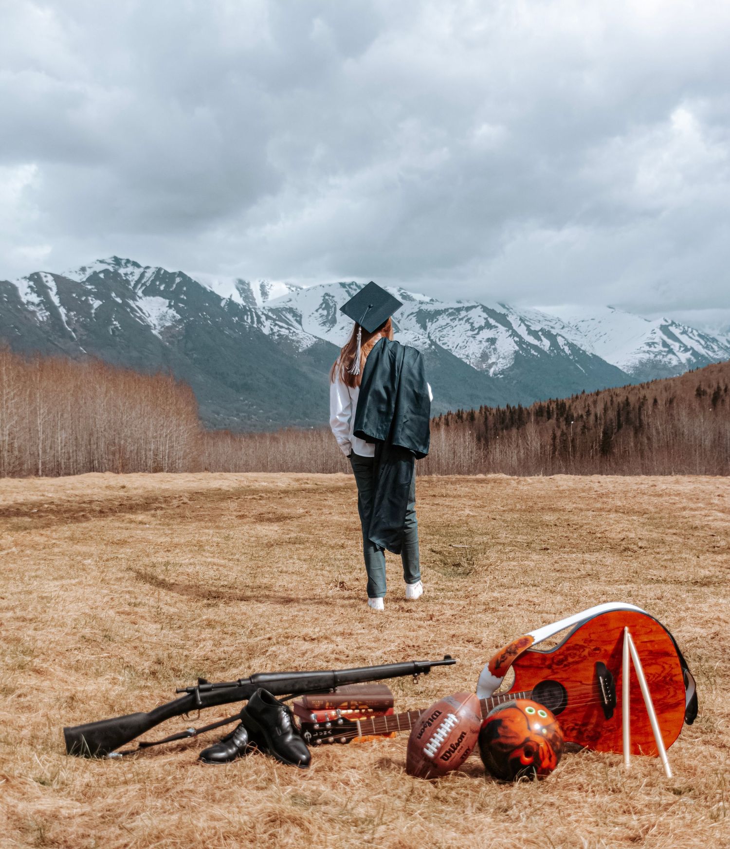Senior portrait of a graduate standing in an open field with sports gear and mountain scenery behind them.