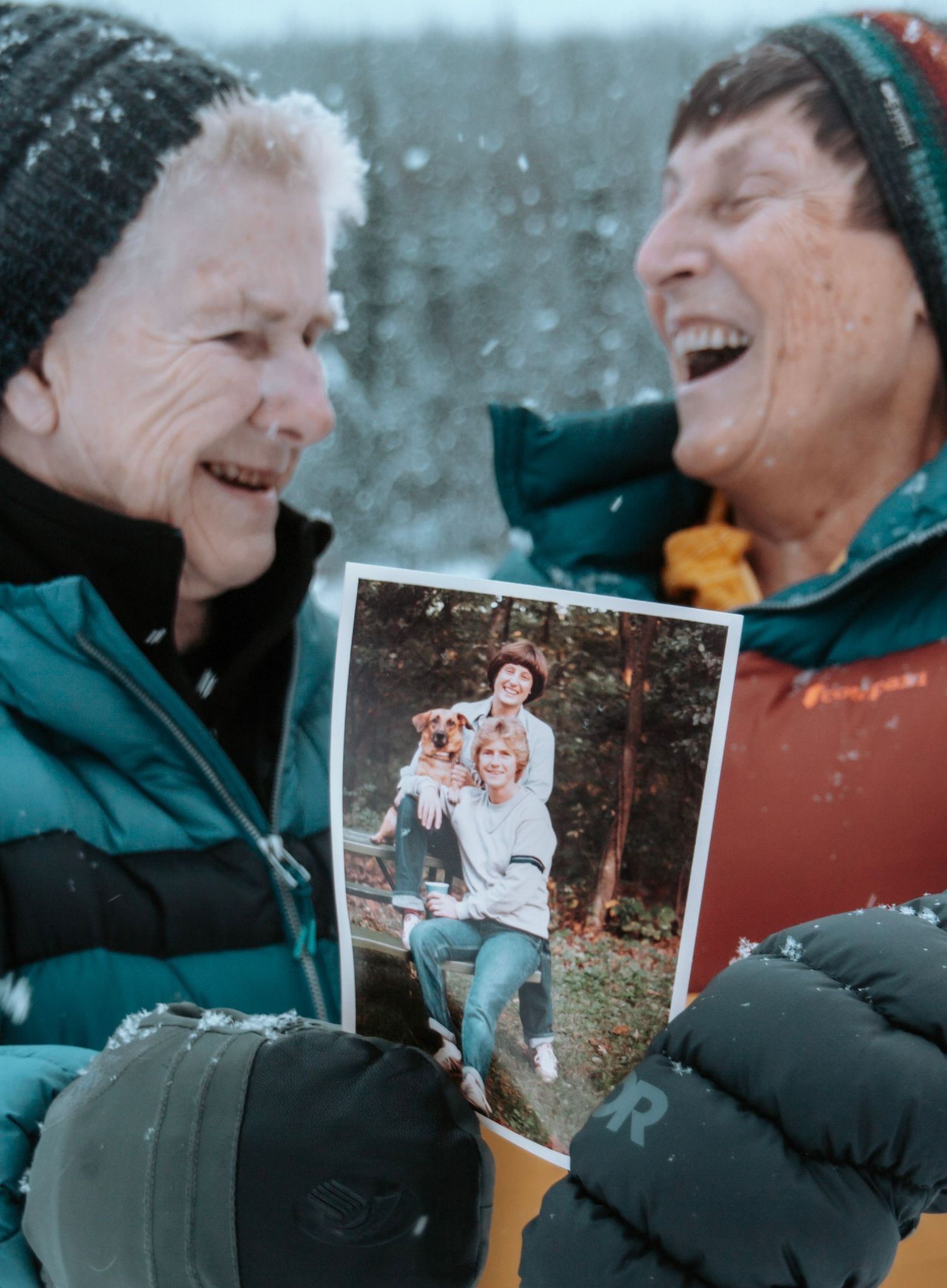 Emotional winter portrait of family members laughing together while holding a printed photo outdoors.
