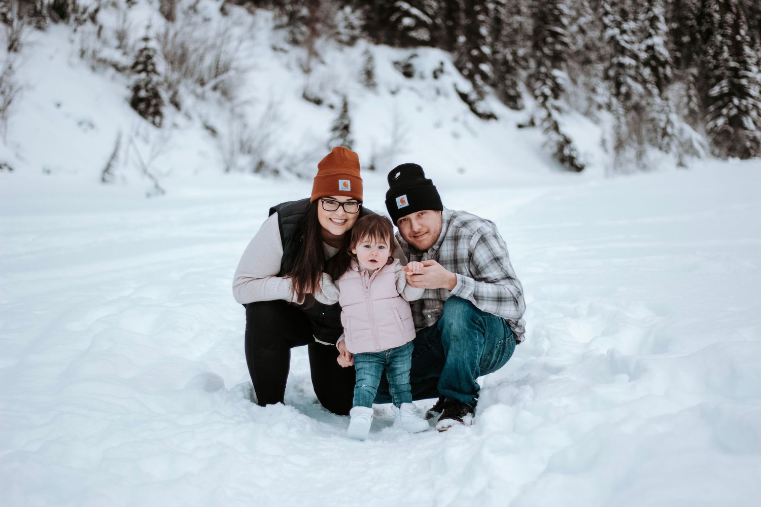 Family with a young child kneeling together in the snow during a cozy winter photography session.
