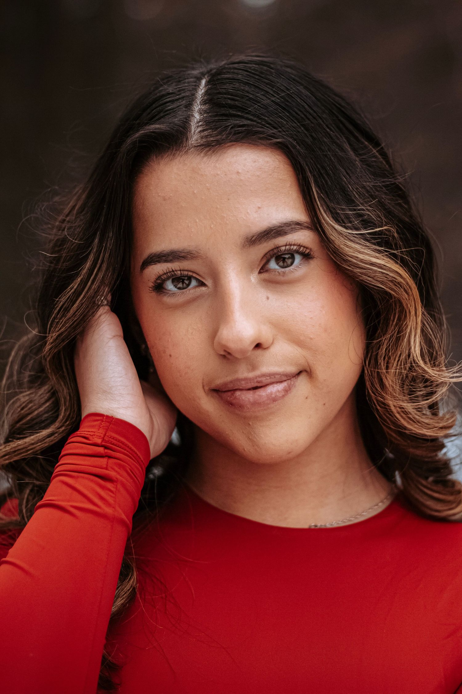 Close-up senior portrait of a young woman in a red top during a natural light outdoor session.