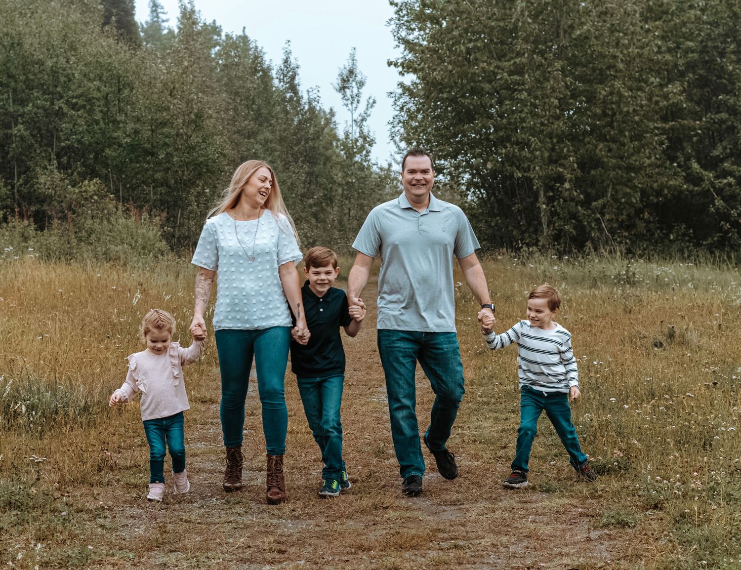 Family of five walking hand in hand through an open field during a natural outdoor photography session.
