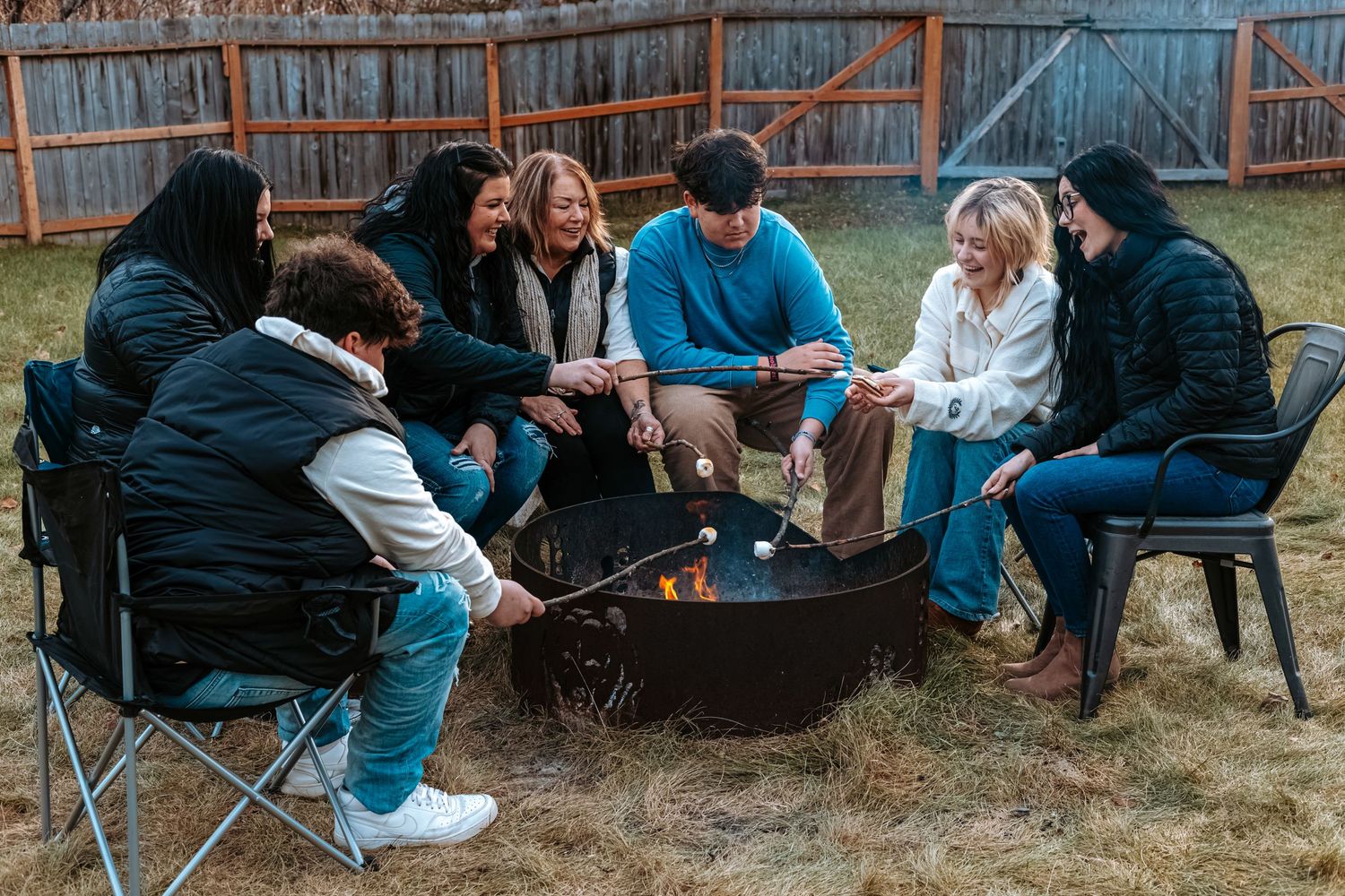 Family members laughing together around a fire pit during a relaxed outdoor lifestyle session.