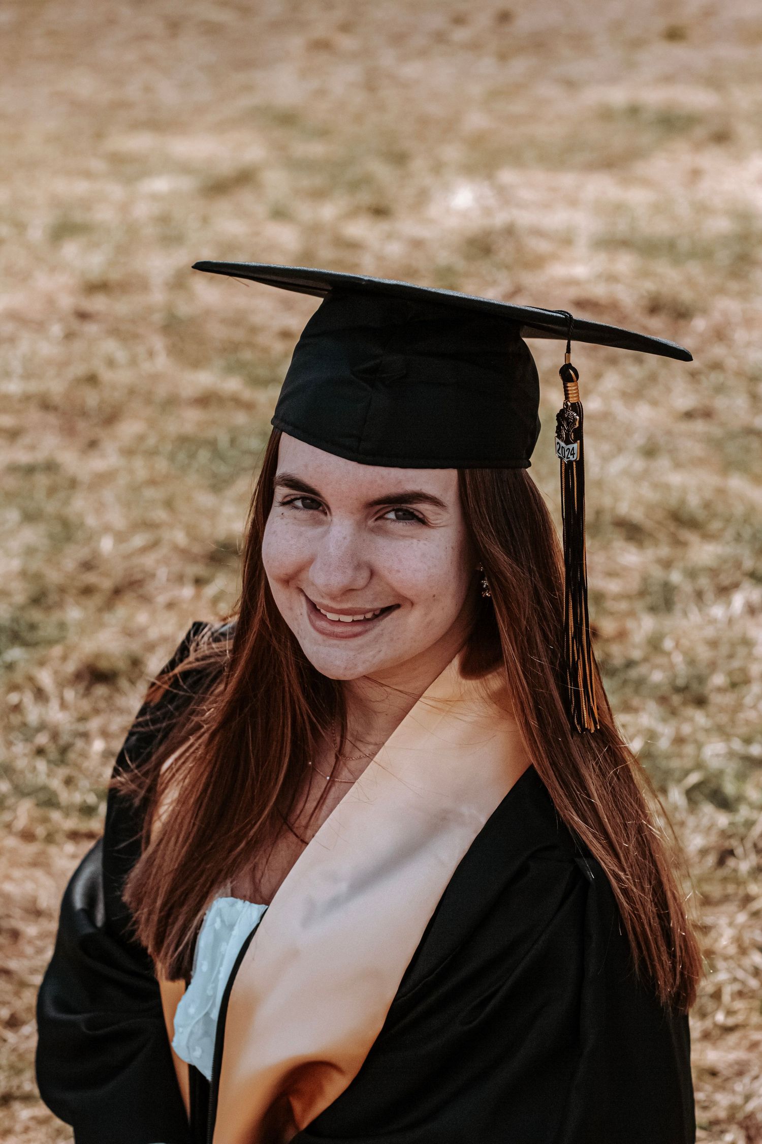 Senior cap and gown portrait of a young woman smiling during an outdoor graduation session.