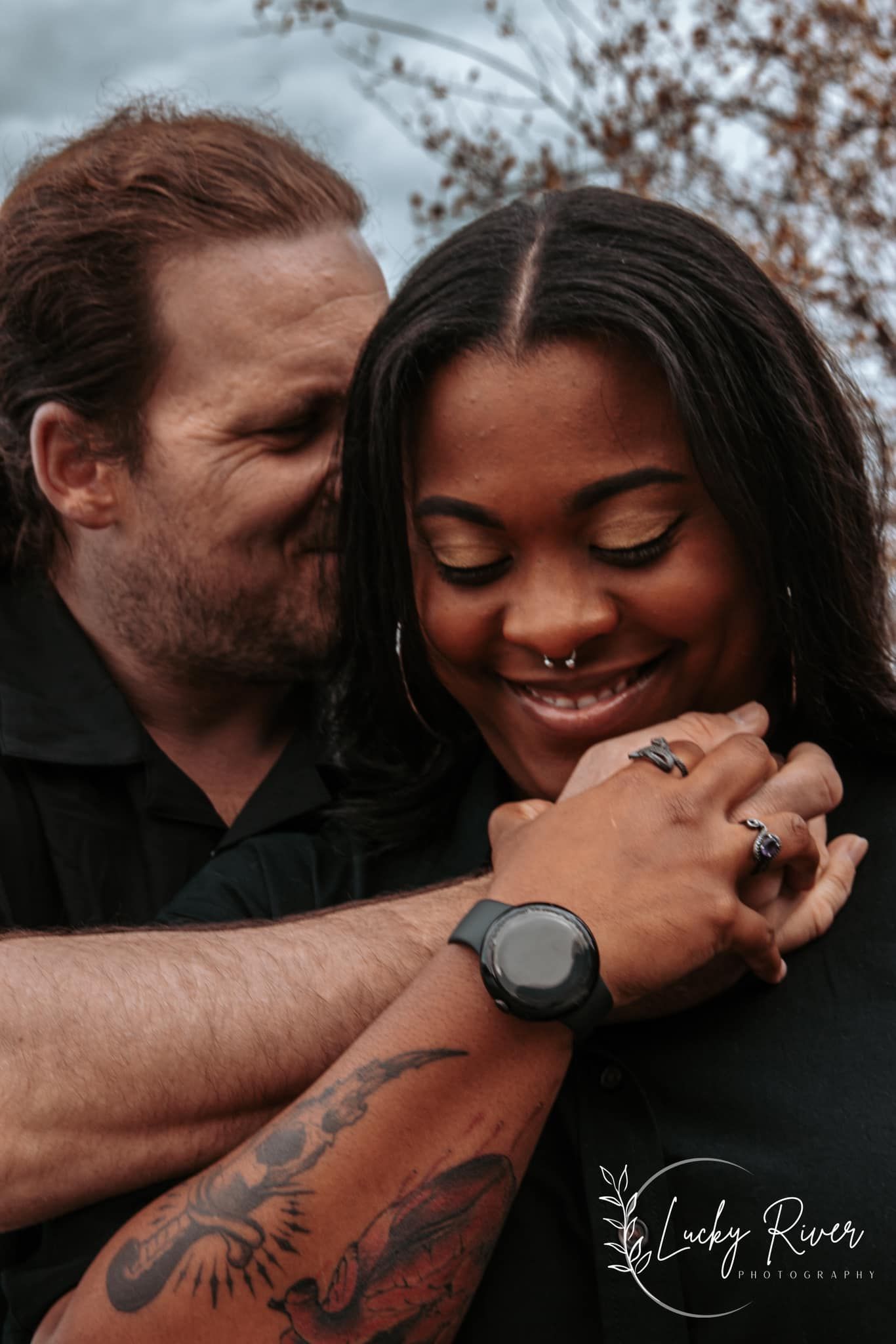 Interracial couple embracing and smiling during an intimate outdoor couples session in Alaska – tattoo and ring details highlighted by LRP