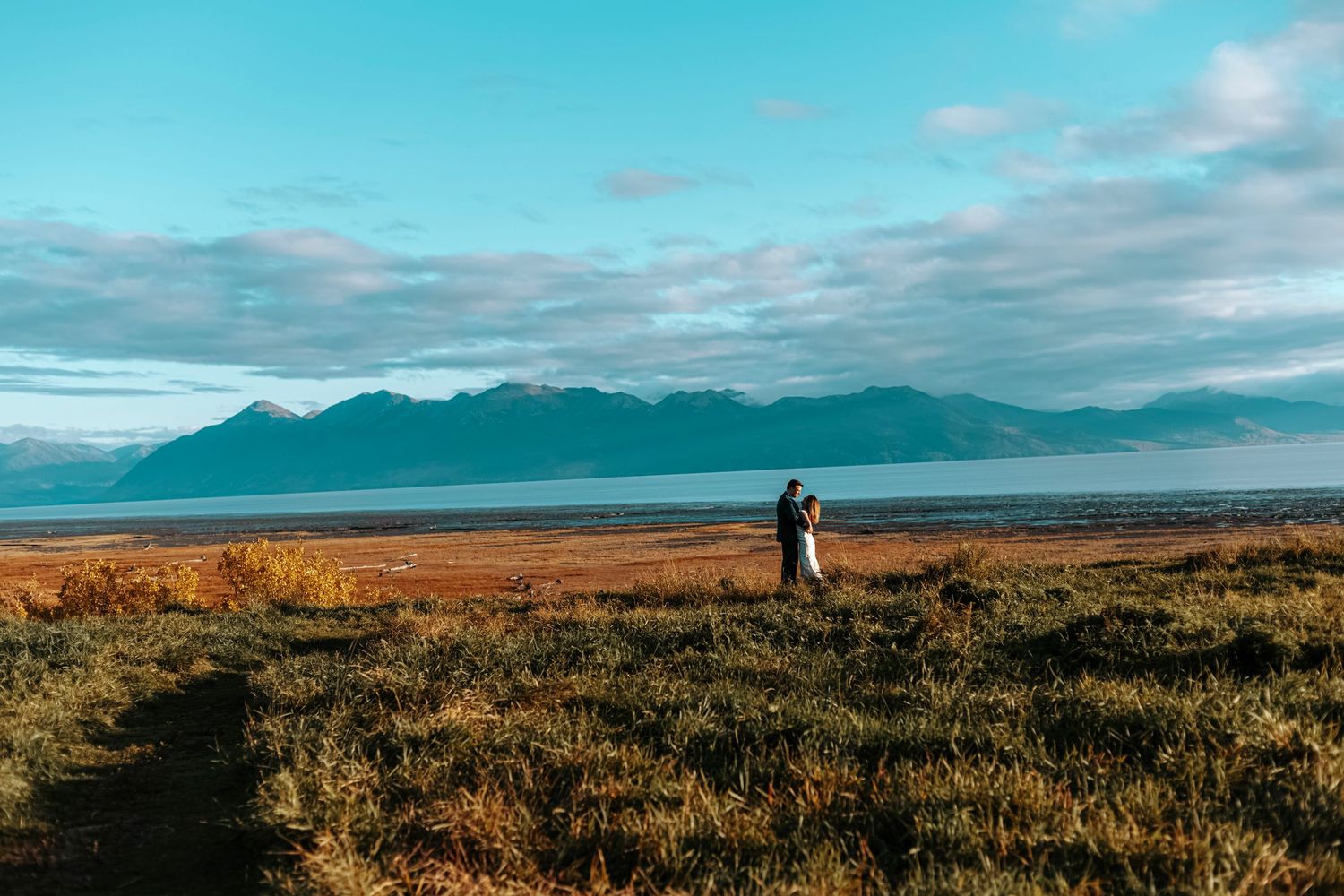 Wide Alaska elopement photo of a couple standing together with mountains and water in the background.
