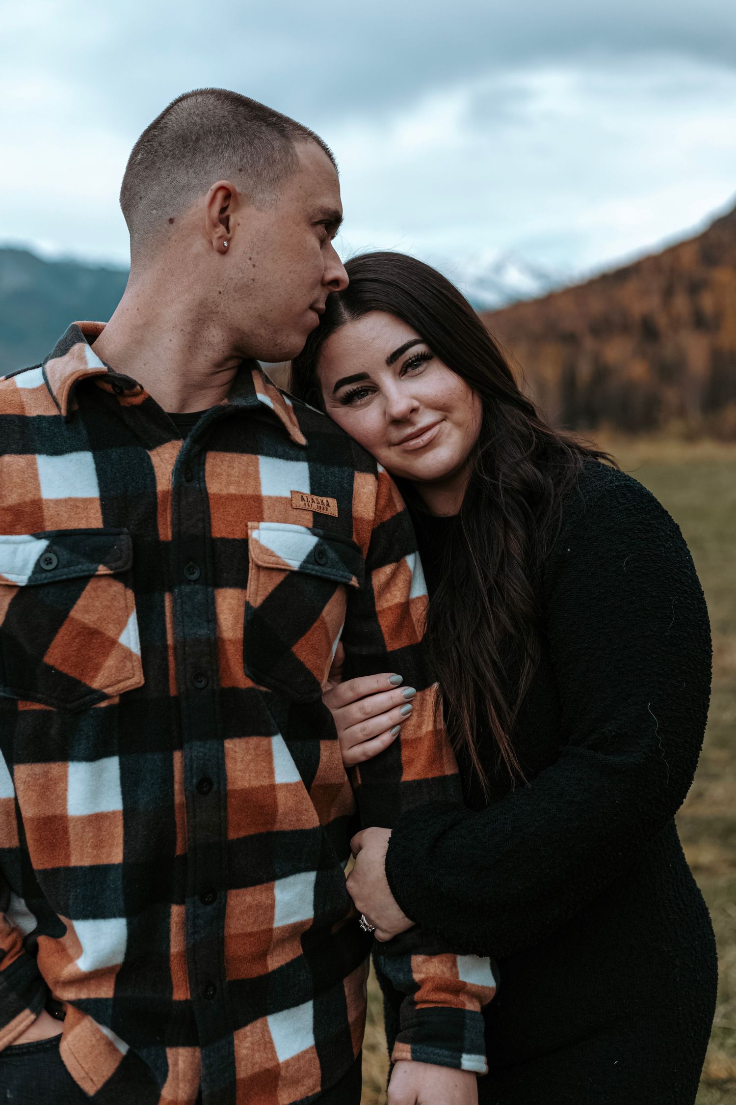 Couple standing close together during an intimate outdoor portrait session with mountain scenery.