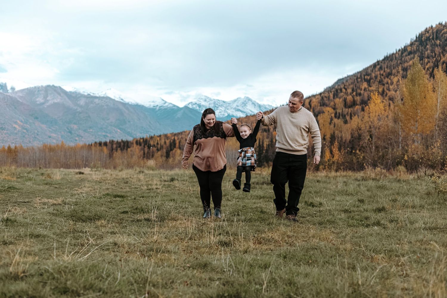 Family walking together through an open field with mountain views during a natural outdoor photo session.