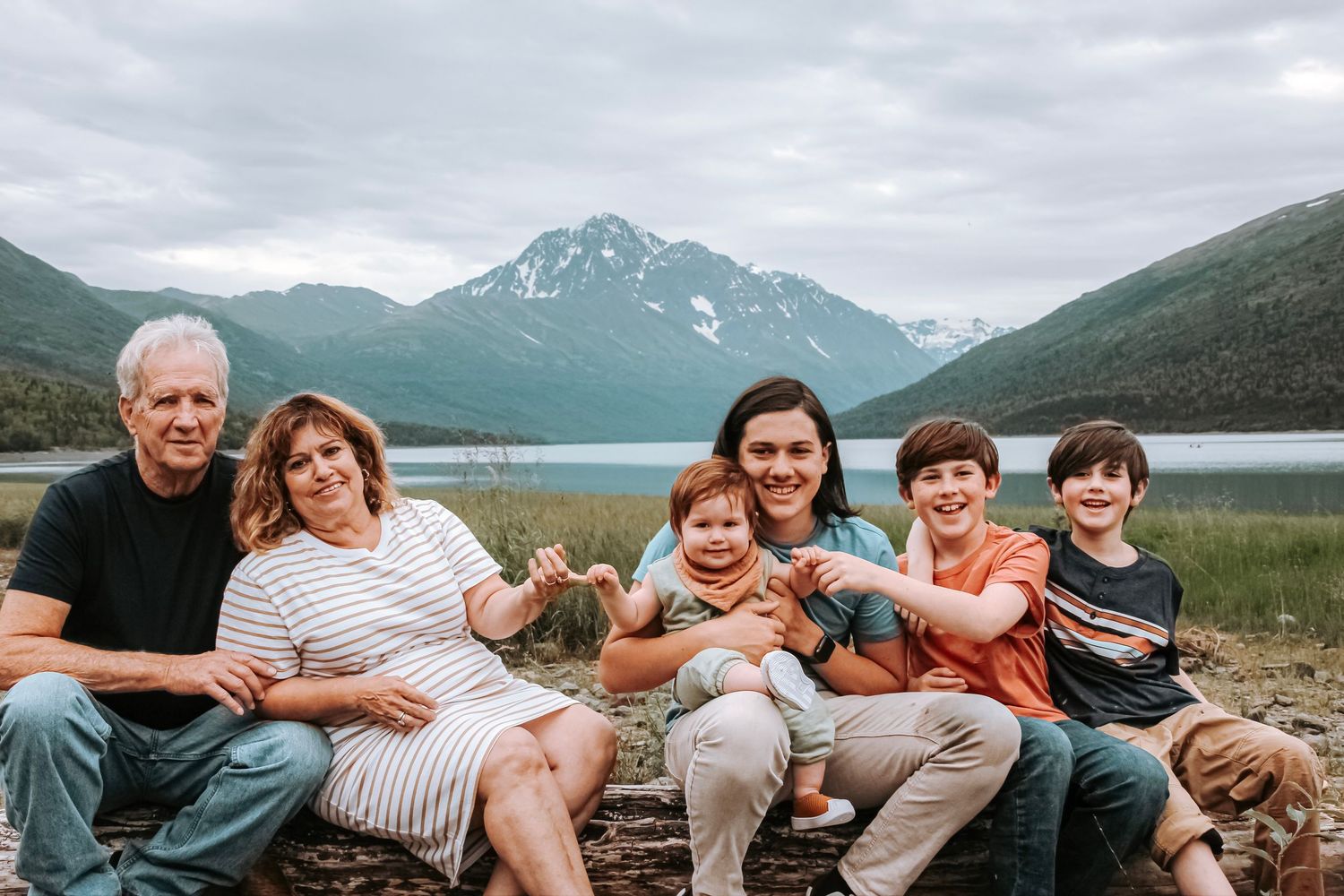 Grandparents and grandchildren smiling in front of a lake and mountains in Alaska