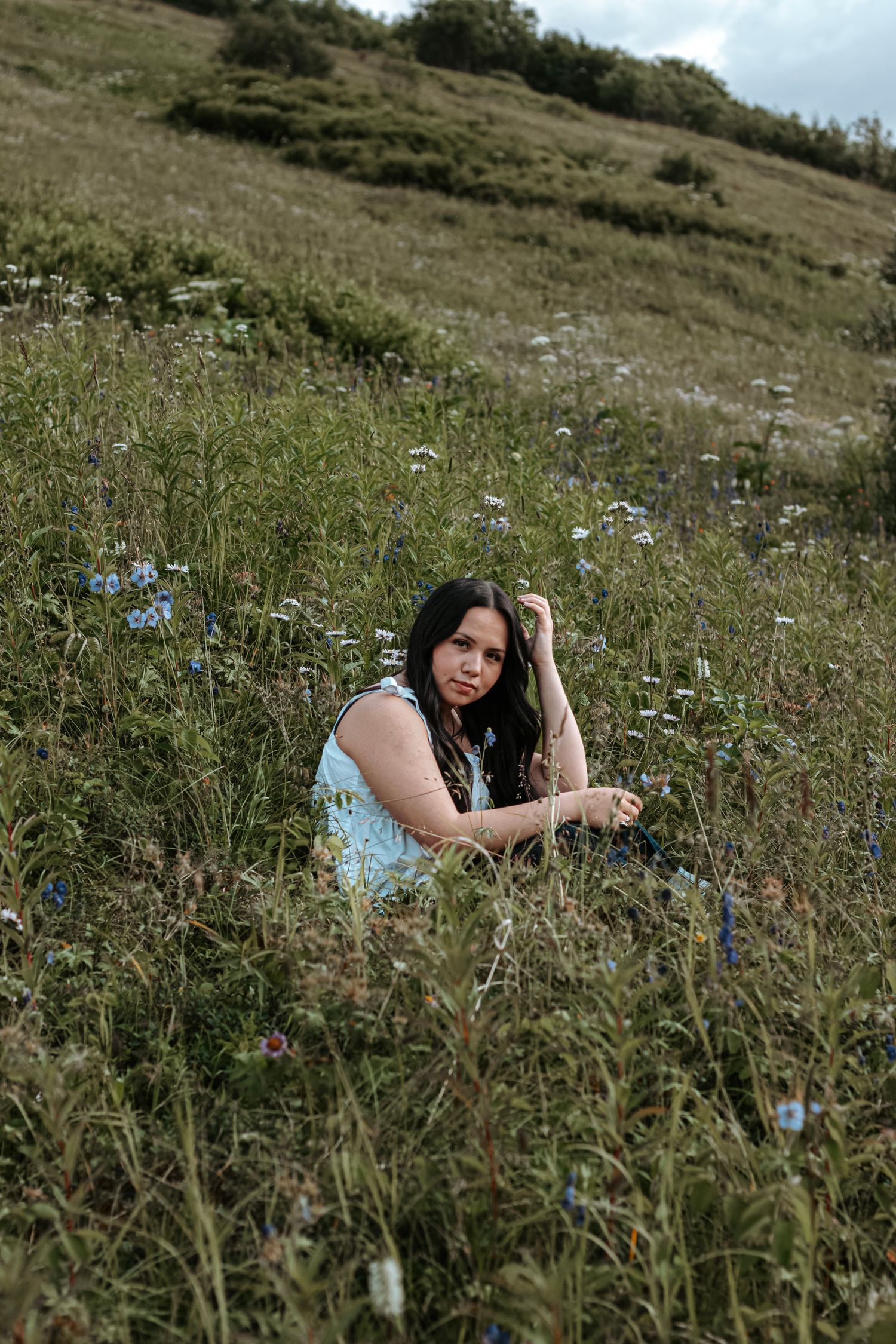 Senior portrait of a young woman sitting in an Alaskan wildflower field during a natural outdoor session.