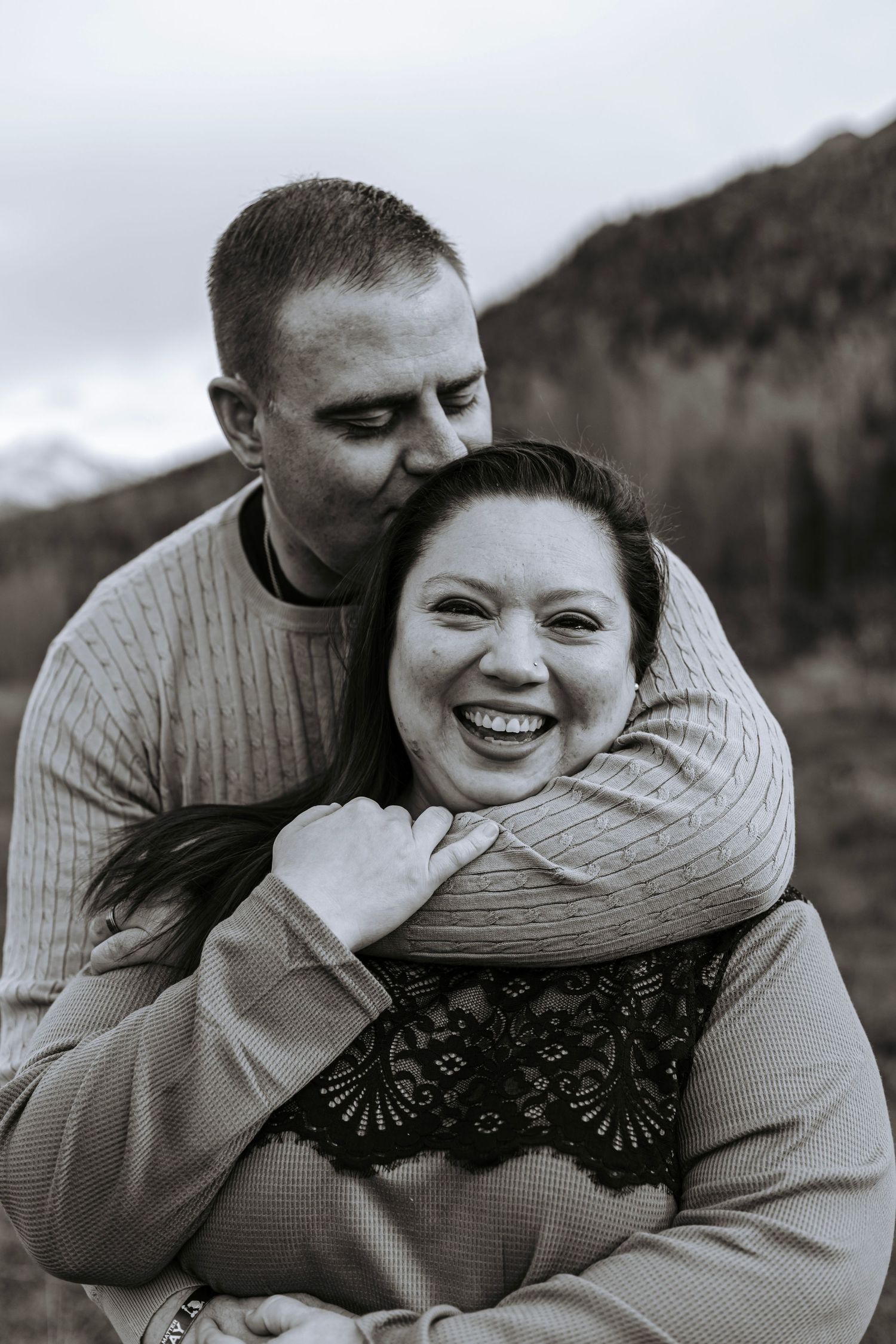 Black and white portrait of a couple laughing while embracing during an outdoor family session.