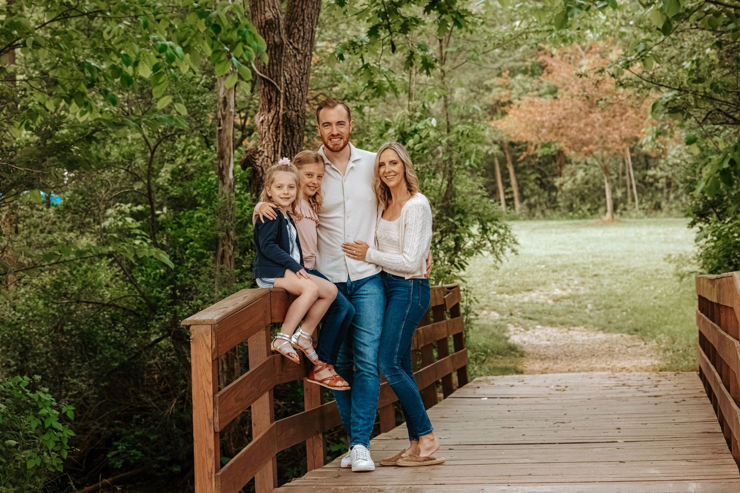 Family of four posing together on a wooden bridge during an outdoor lifestyle photography session.