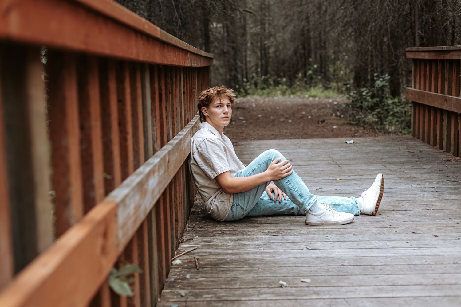 Senior portrait of a young man sitting on a wooden bridge during a relaxed outdoor session in Alaska.
