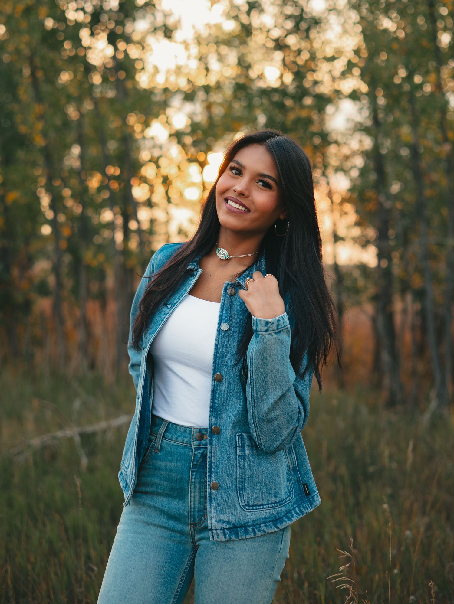 senior in denim jacket poses thoughtfully against golden sunset in wooded area during autumn season. photo, Great Falls, MT