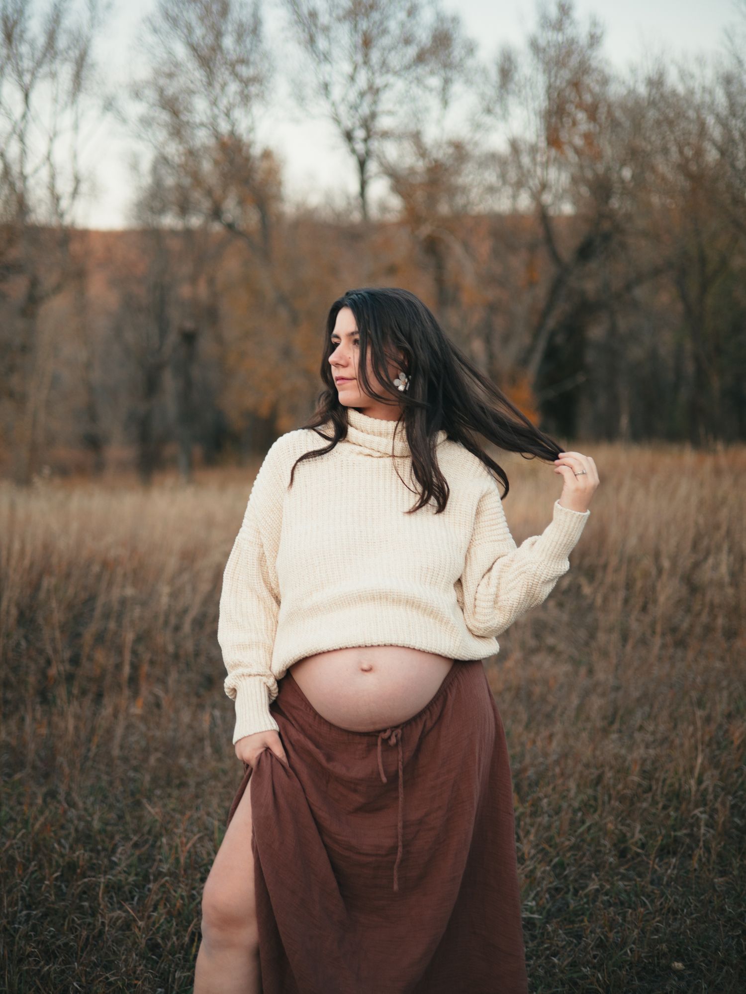Maternity photo series showing a pregnant woman in a cream sweater and brown skirt standing in a rustic autumn field. photo, Great Falls, MT