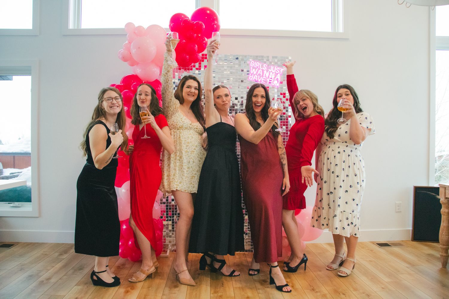 Women celebrating together under pink balloon decorations in a bright indoor space. Great Falls, Montana