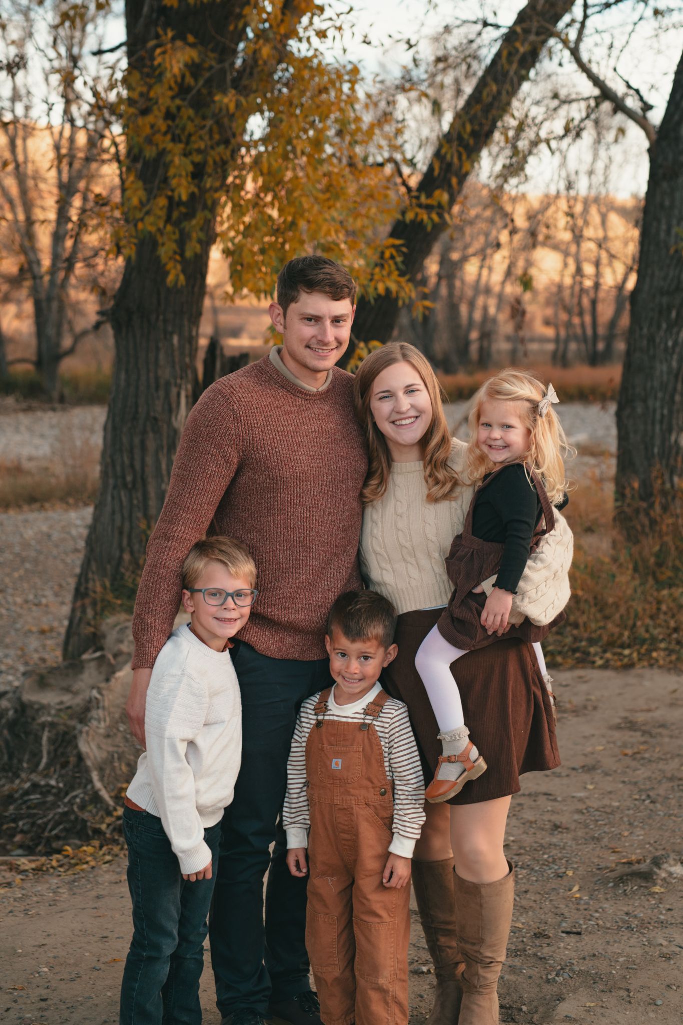 A family of five poses together outdoors on an autumn day with fall foliage and trees in the background. photo, Great Falls, MT