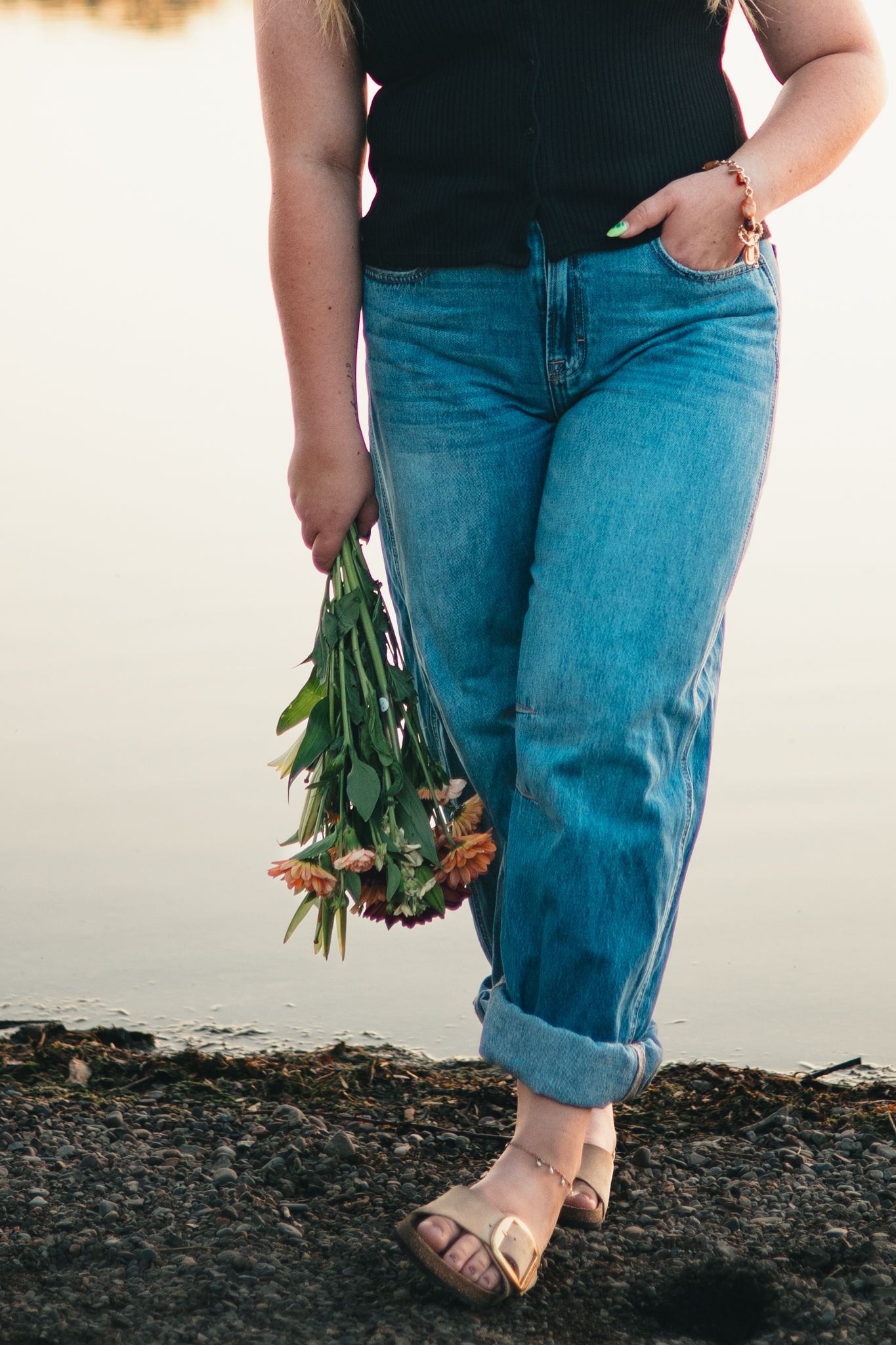 Senior wearing blue jeans and brown sandals holds fresh green onions while standing on dark soil. photo, Great Falls, MT